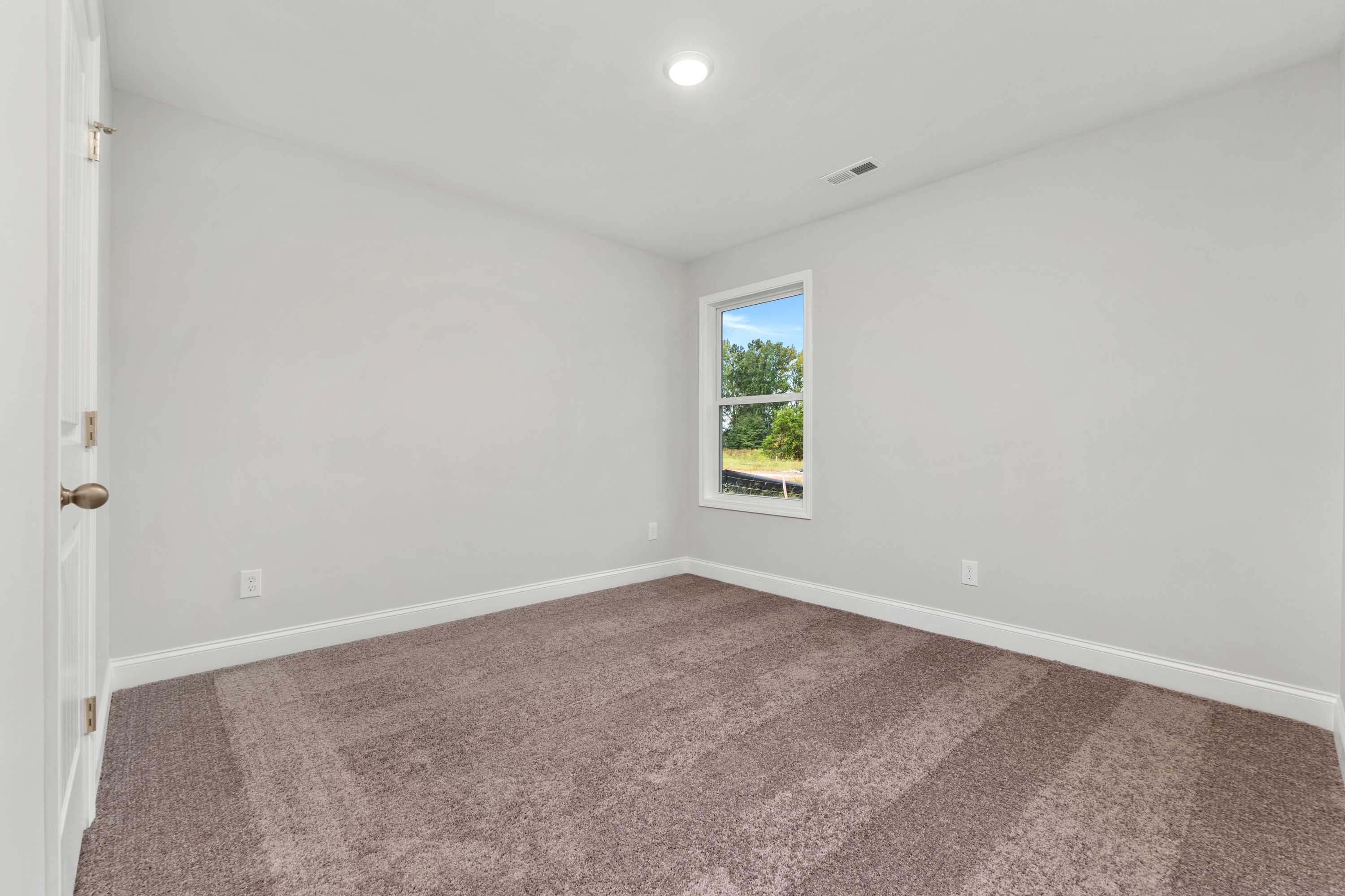 Bright bedroom interior at Collins Lane in Meridianville, Alabama with light gray walls, plush carpet, and large window overlooking greenery