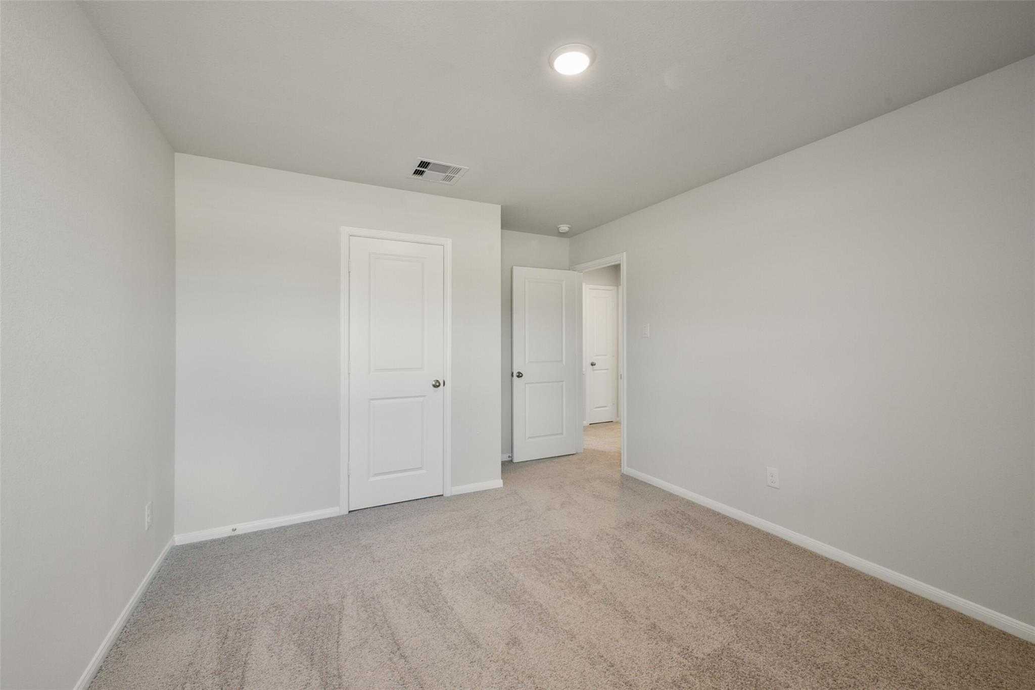 Empty bedroom with white walls, beige carpet, walk-in closet door, and en-suite access in Davidson Homes The Sabine E, Dayton, Texas