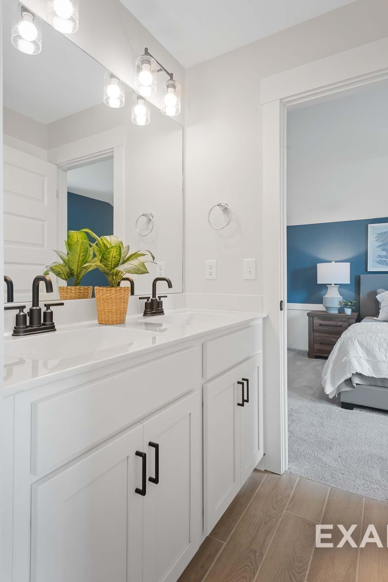 Modern double vanity bathroom with white shaker cabinets, black faucets, and potted plant, open to master suite in Davidson Homes The Ridgeport C, Gallatin, TN