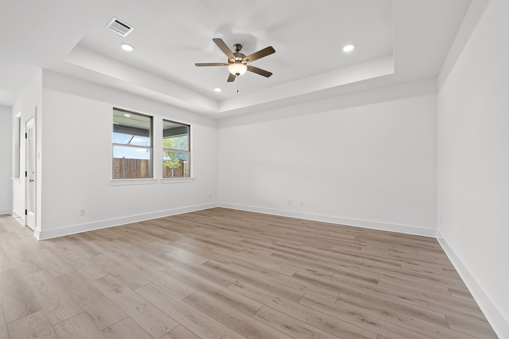 Bright bedroom with tray ceiling, ceiling fan, and wood-look flooring in Davidson Homes The Holly F, Meadow Ridge Estates, Josephine, TX