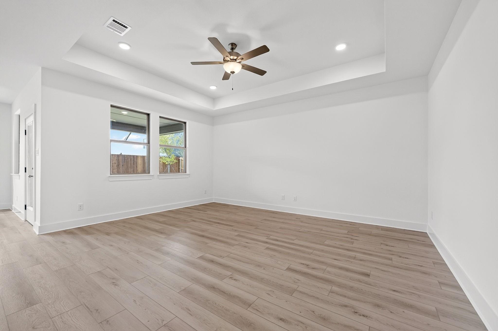 Bright bedroom with tray ceiling, ceiling fan, and wood-look flooring in Davidson Homes The Holly F, Meadow Ridge Estates, Josephine, TX