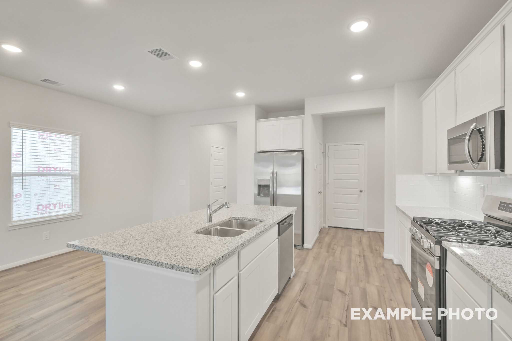 Kitchen with granite island, stainless steel appliances, and white cabinetry in The Brazos by Davidson Homes, Beasley, TX
