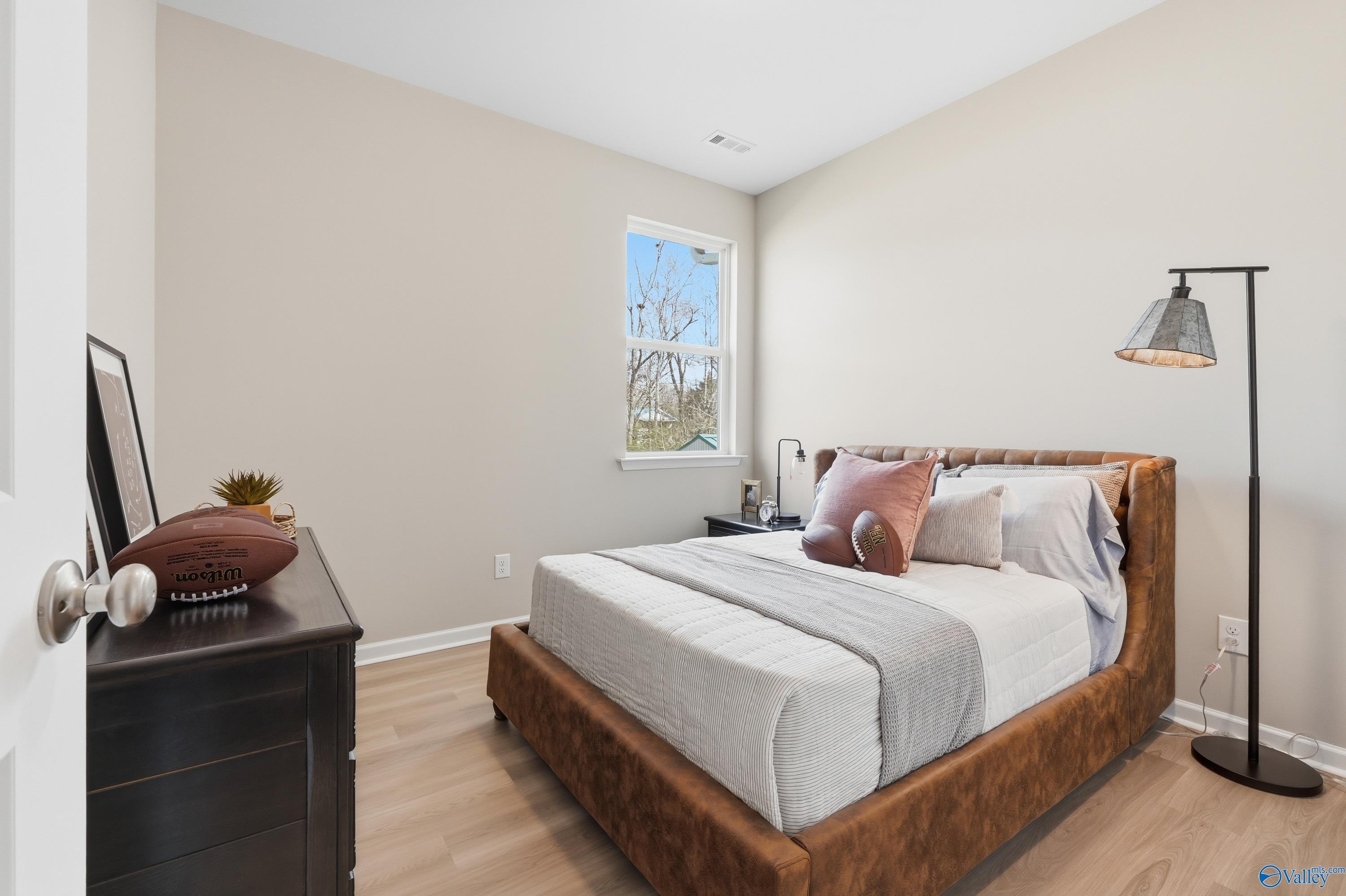 Cozy bedroom with upholstered bed, pink pillows, nightstand lamp, and window view in Davidson Homes The Polaris, Fayetteville, Tennessee