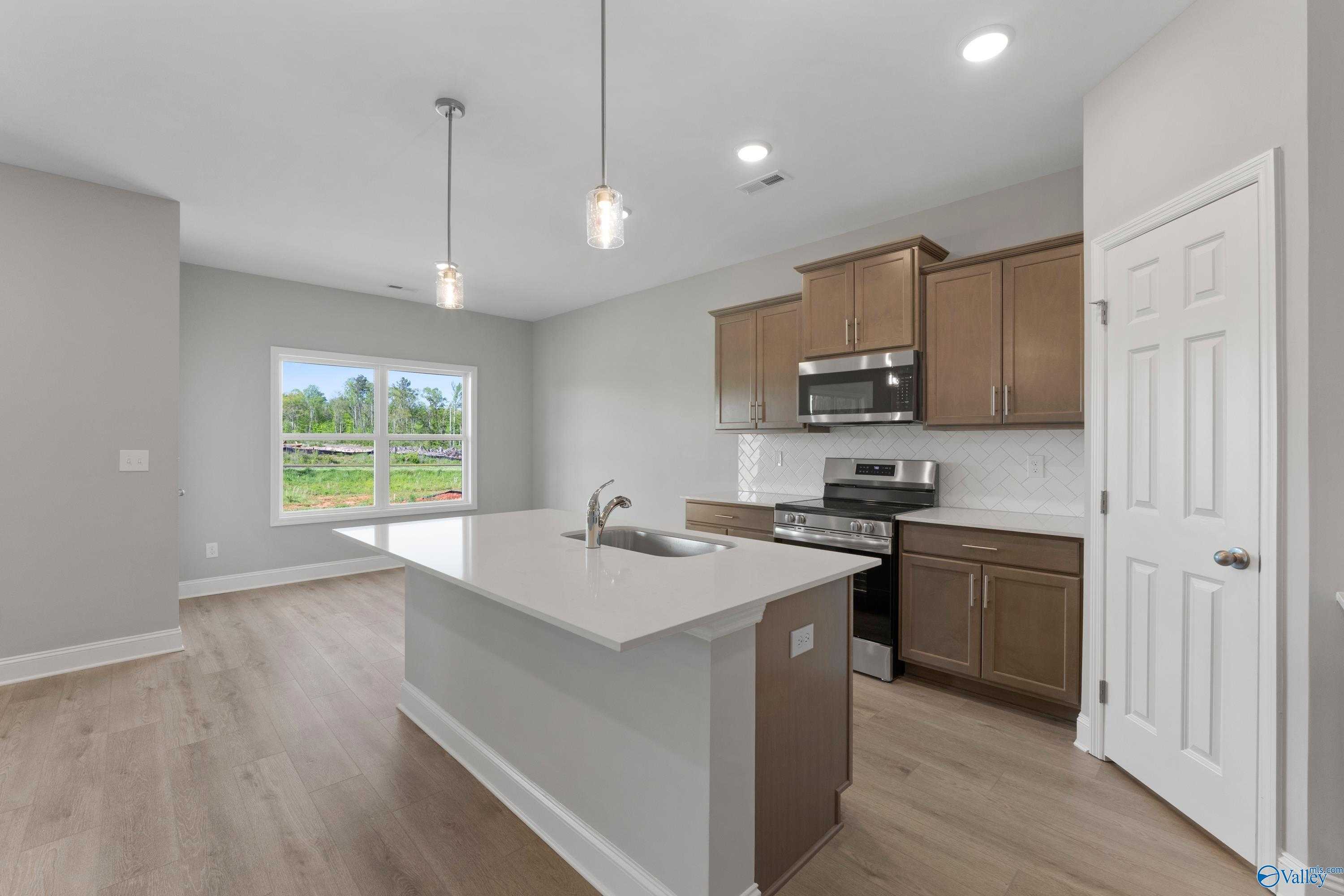 Modern kitchen with white quartz island sink, stainless appliances, wood cabinets, and garden view window in Davidson Homes The Asheville C, Athens AL