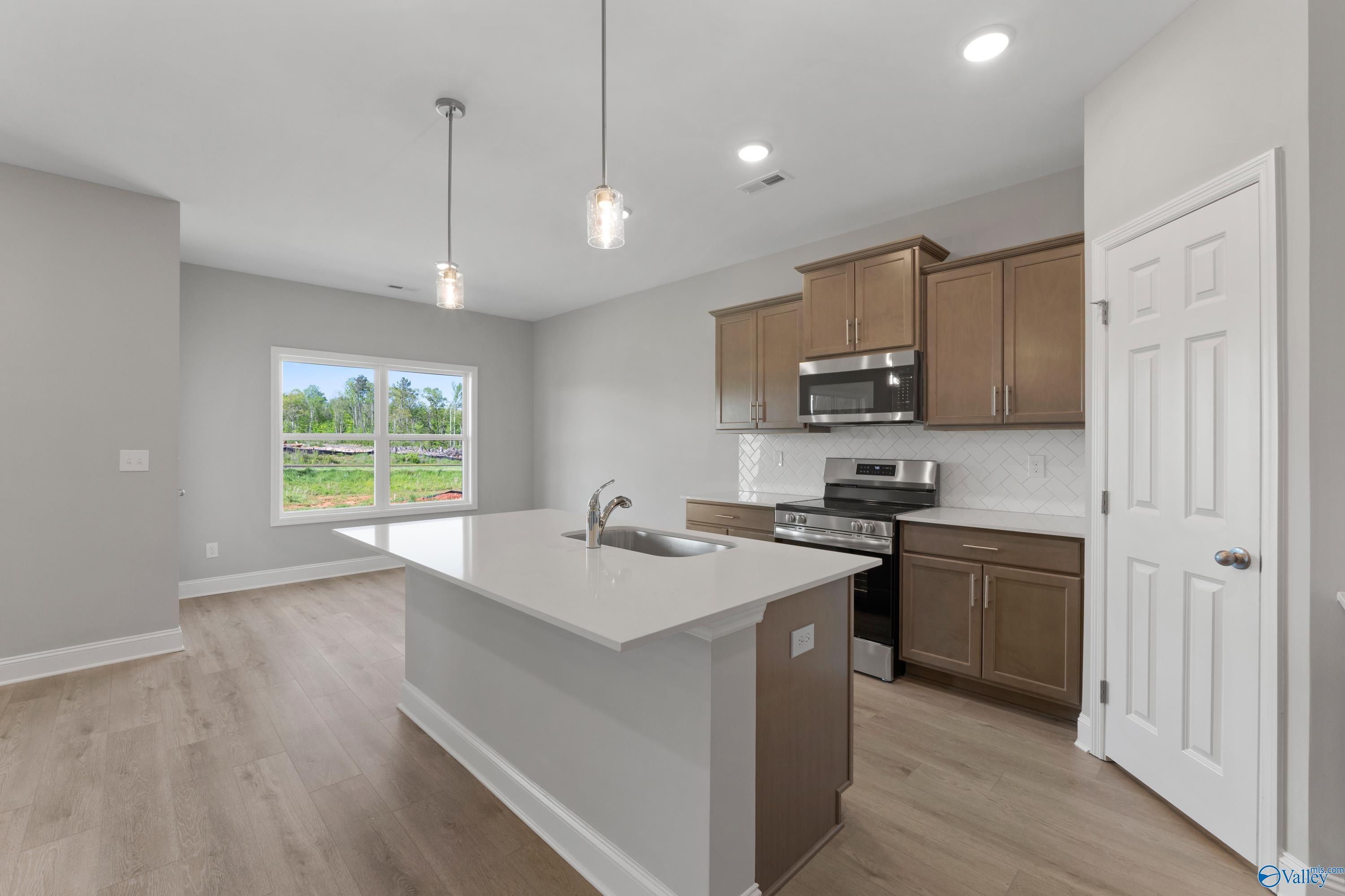 Modern kitchen with white quartz island sink, stainless appliances, wood cabinets, and garden view window in Davidson Homes The Asheville C, Athens AL