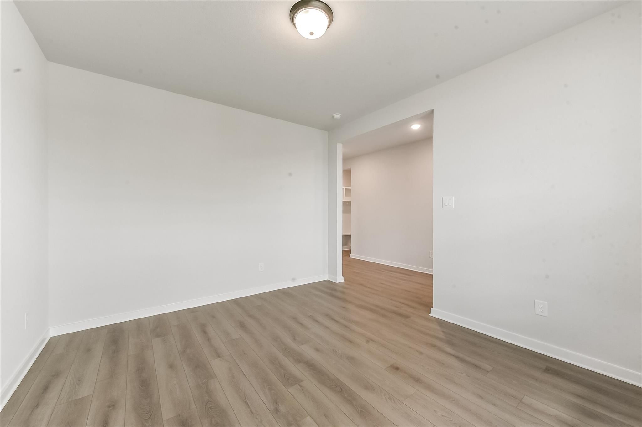 Spacious empty bedroom with light wood laminate flooring, white walls, and arched closet entry in Davidson Homes The Everett C, Crosby, Texas