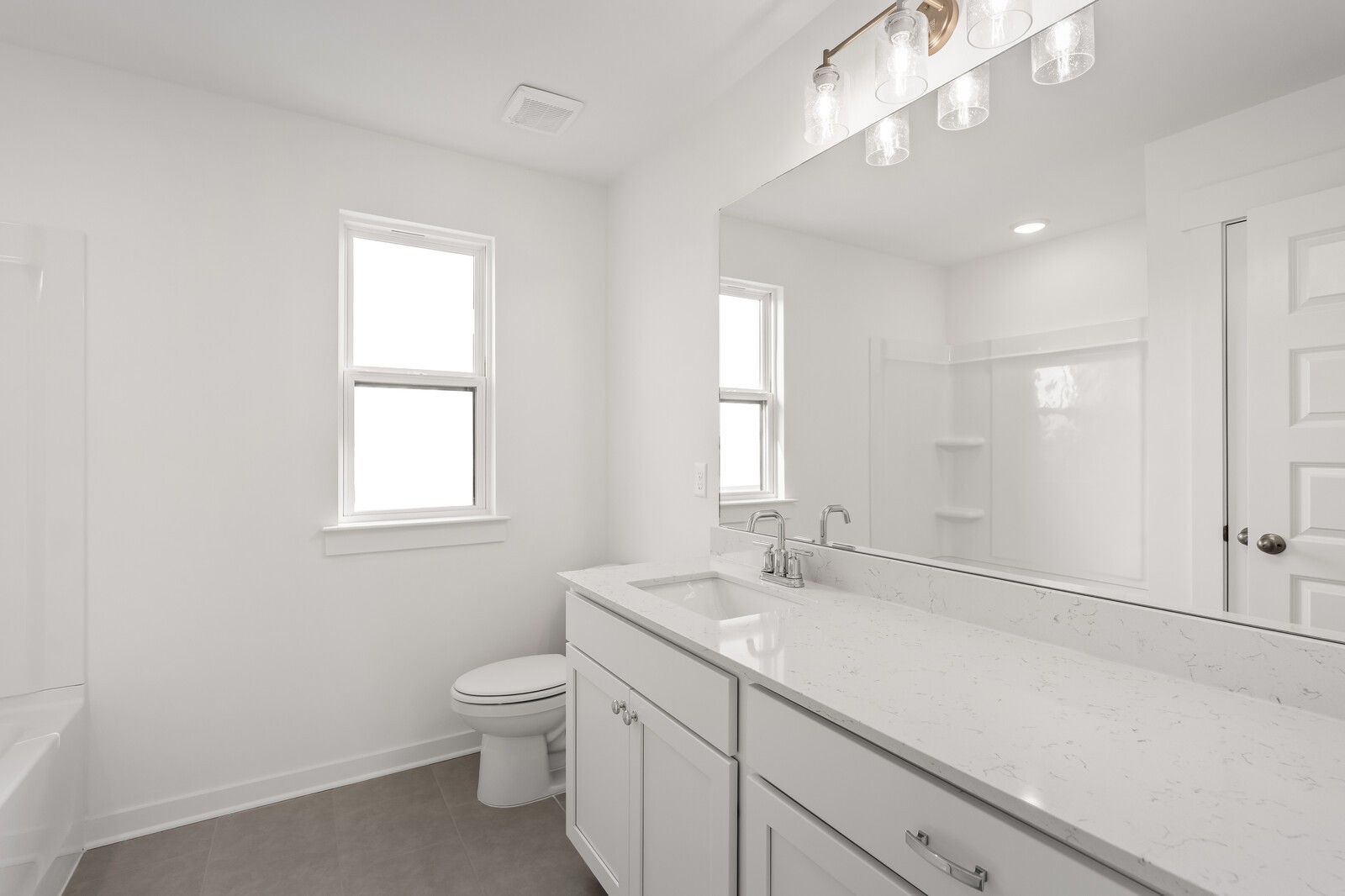 Modern white guest bathroom with quartz countertop vanity, large mirror, and enclosed shower in Davidson Homes The Willow D, Mt. Juliet