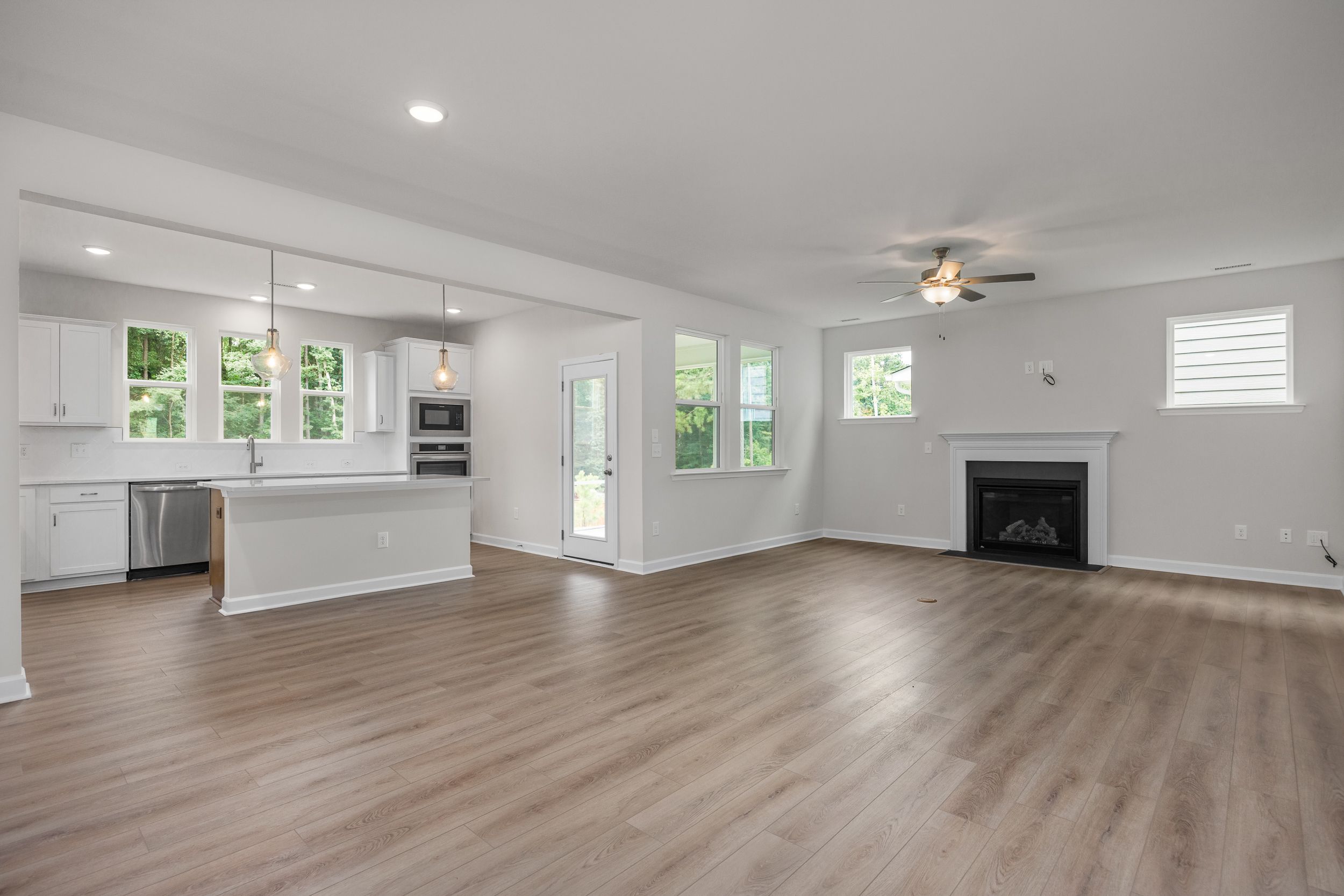 Spacious open-concept kitchen and great room in The Aspen home featuring white cabinets, large island, fireplace, and hardwood floors