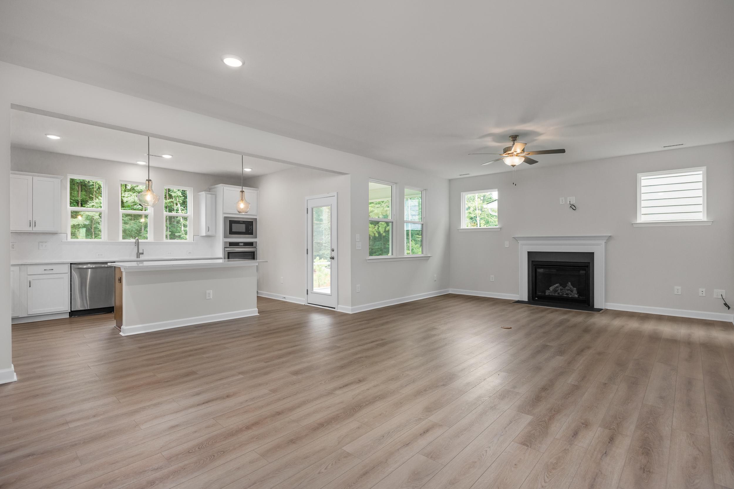 Spacious open-concept kitchen and great room in The Aspen home featuring white cabinets, large island, fireplace, and hardwood floors