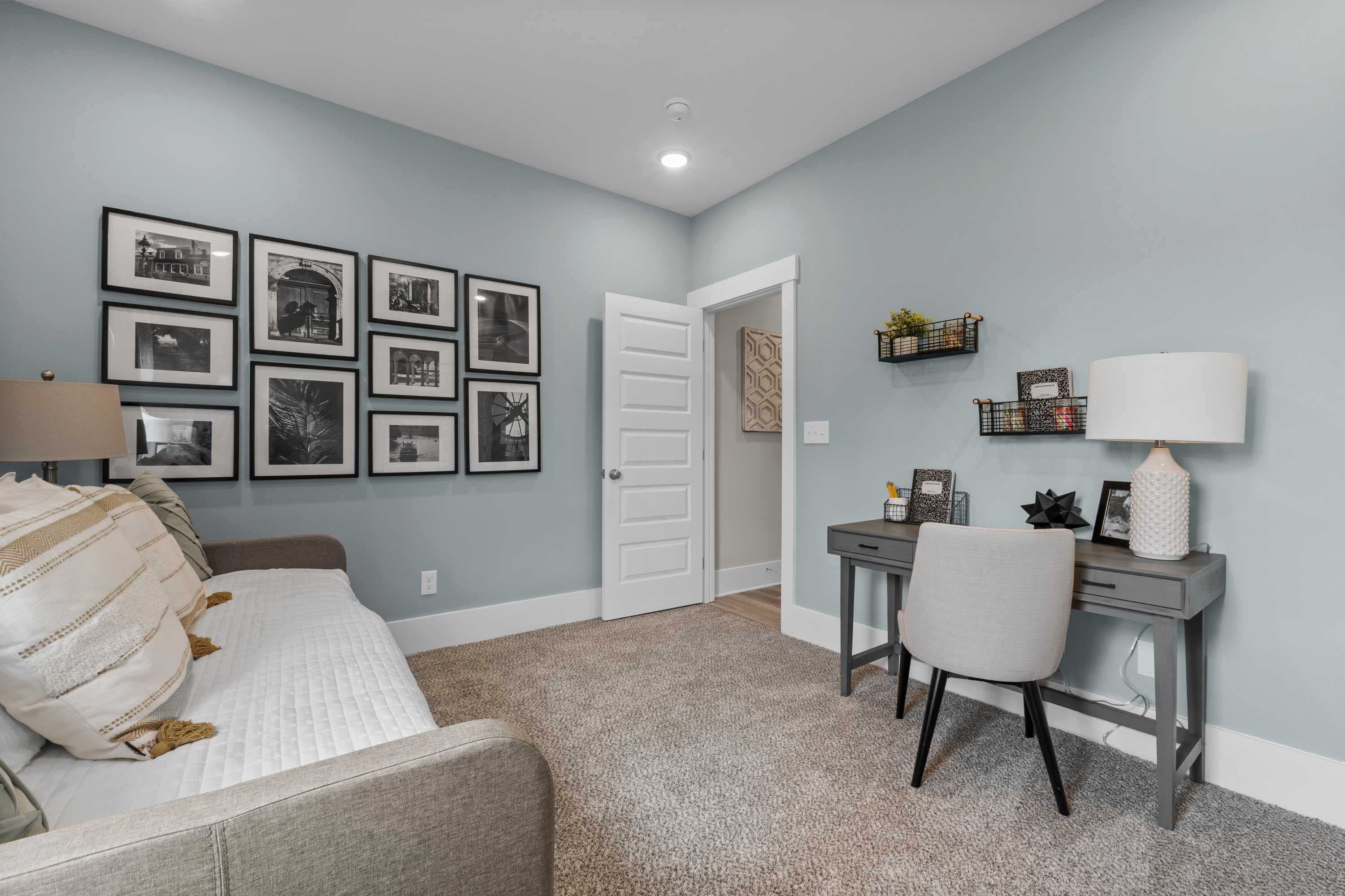 Cozy home office in The Highlands Arab Alabama with light blue walls, gray desk, chair, framed photos, shelves, and daybed sofa
