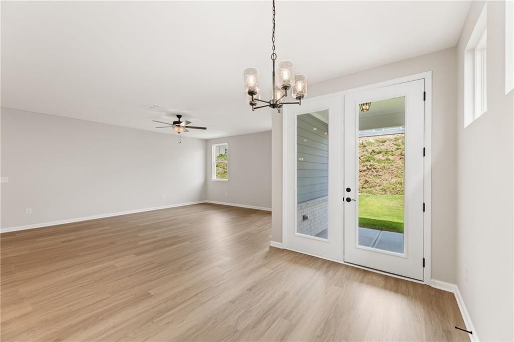 Bright living room with hardwood floors, chandelier, ceiling fan, and French doors to green backyard in Davidson Homes The Daphne C, Loganville, GA