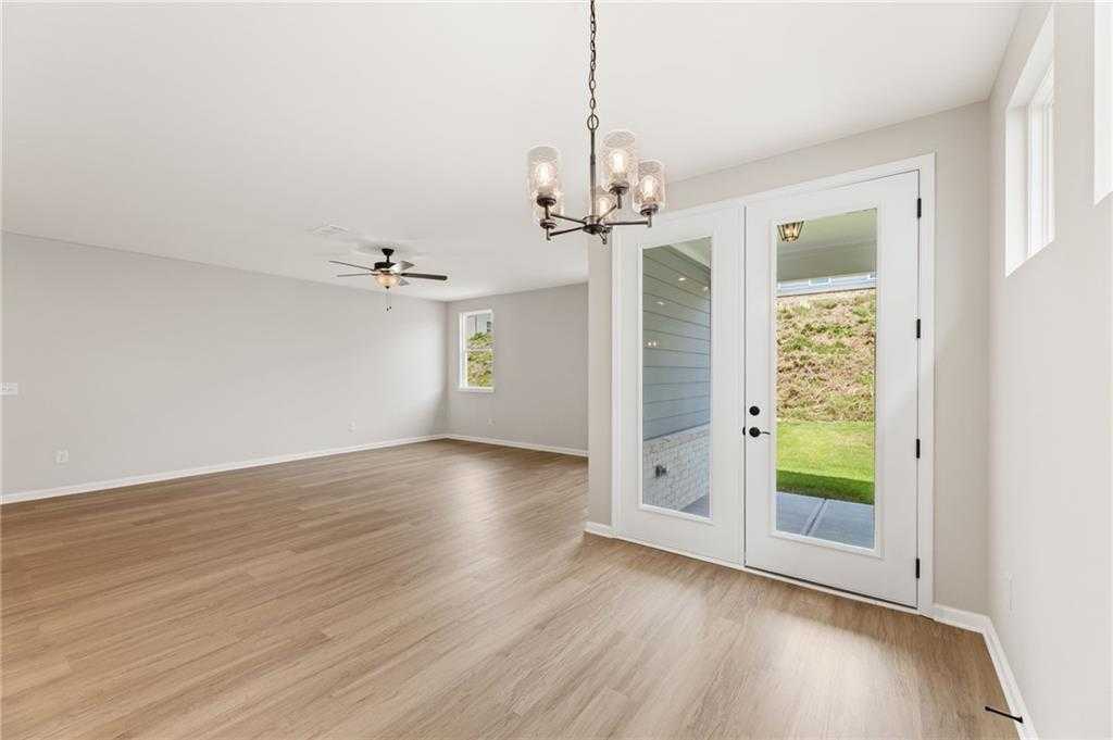 Spacious living room with light hardwood floors, ceiling fan, chandelier, and French doors to green backyard in The Daphne C floor plan, Loganville, GA