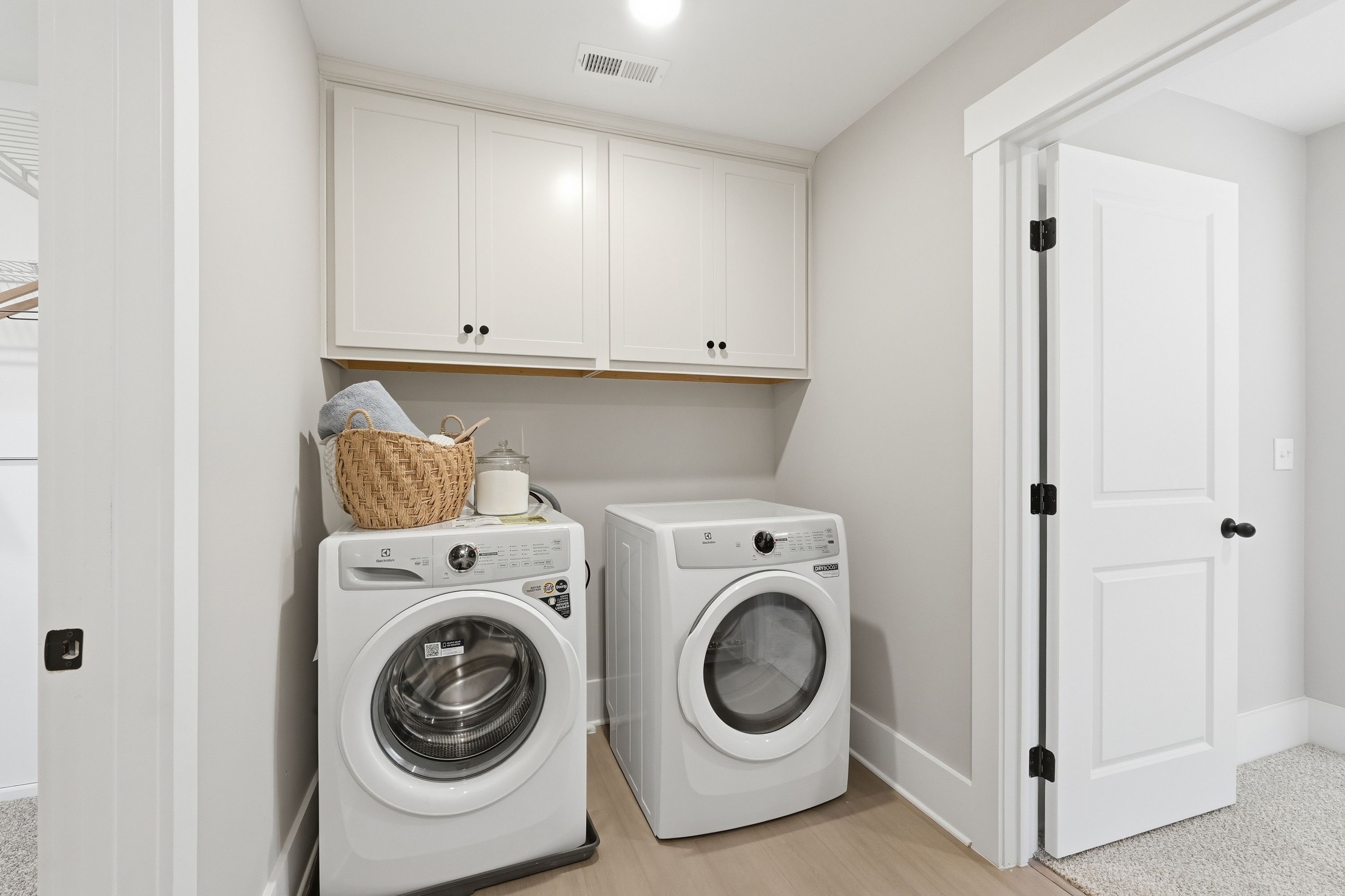 Spacious laundry room in Berry Cove, New Market Alabama with white washer dryer, wicker basket and upper cabinets