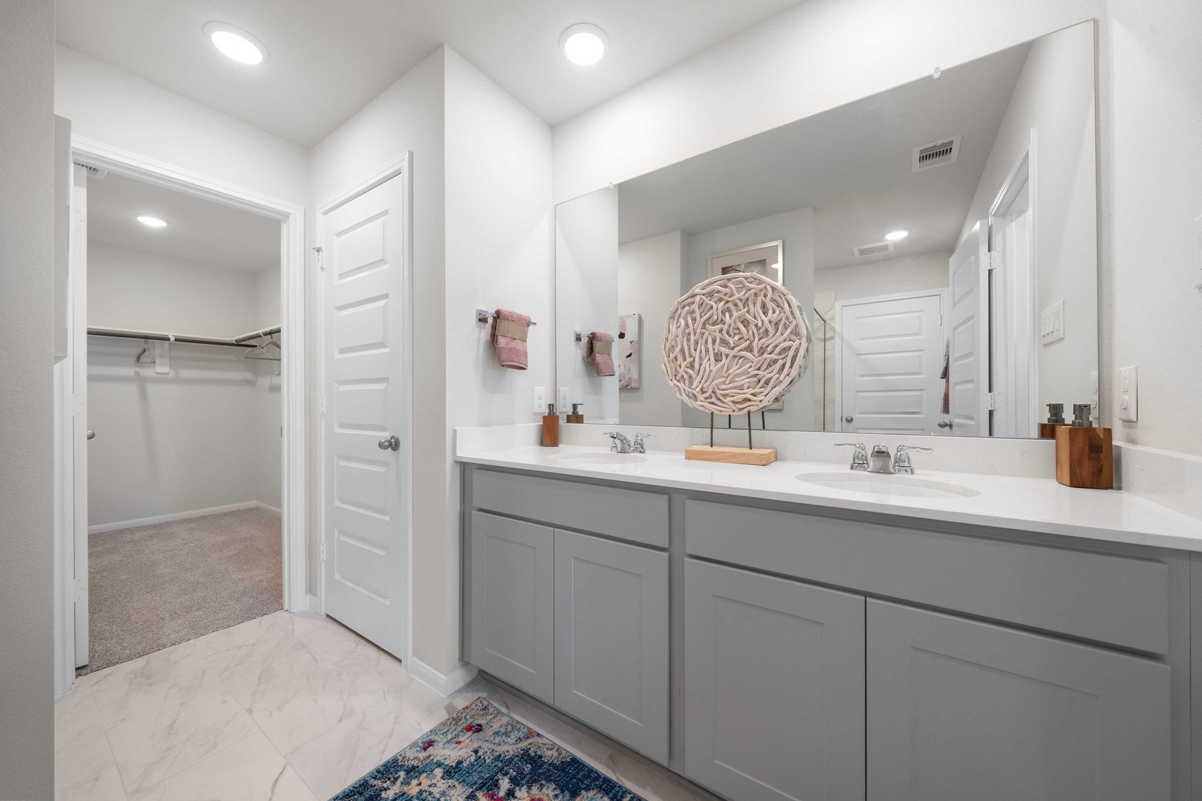 Spacious primary bathroom at Hill & Dale Ranch in Splendora, Texas with double gray vanity, quartz countertop, and walk-in closet