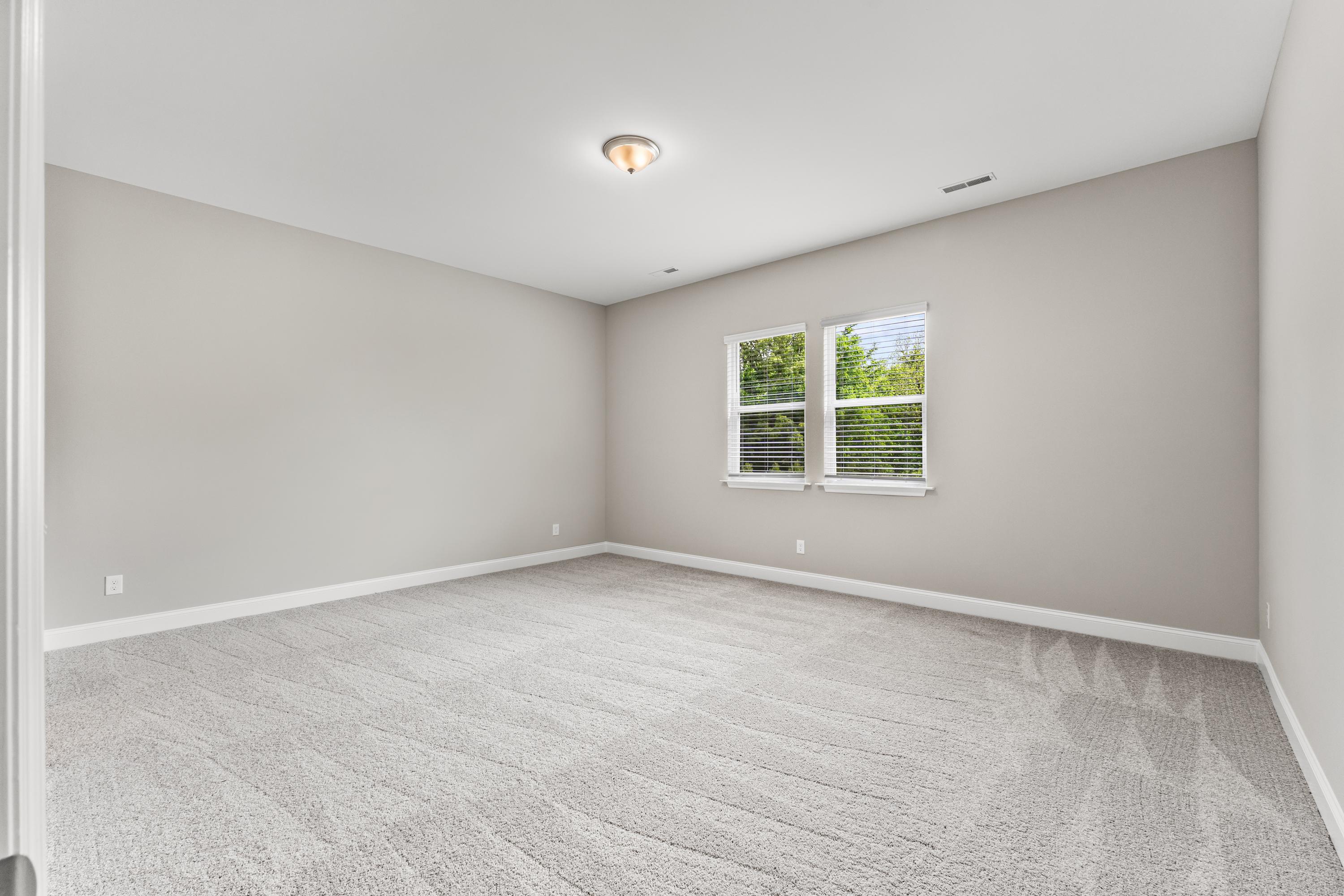 Spacious bedroom in The Arcadia B by Evermore Homes featuring light gray walls, beige carpet, and large windows with blinds