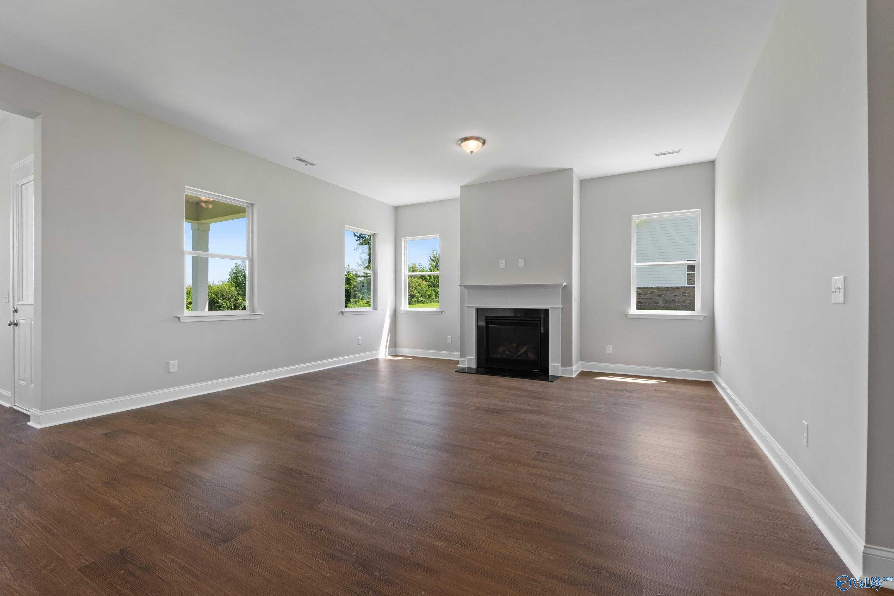 Spacious living room featuring stone fireplace, hardwood floors, and large windows in Davidson Homes The Arcadia, Huntsville, Alabama