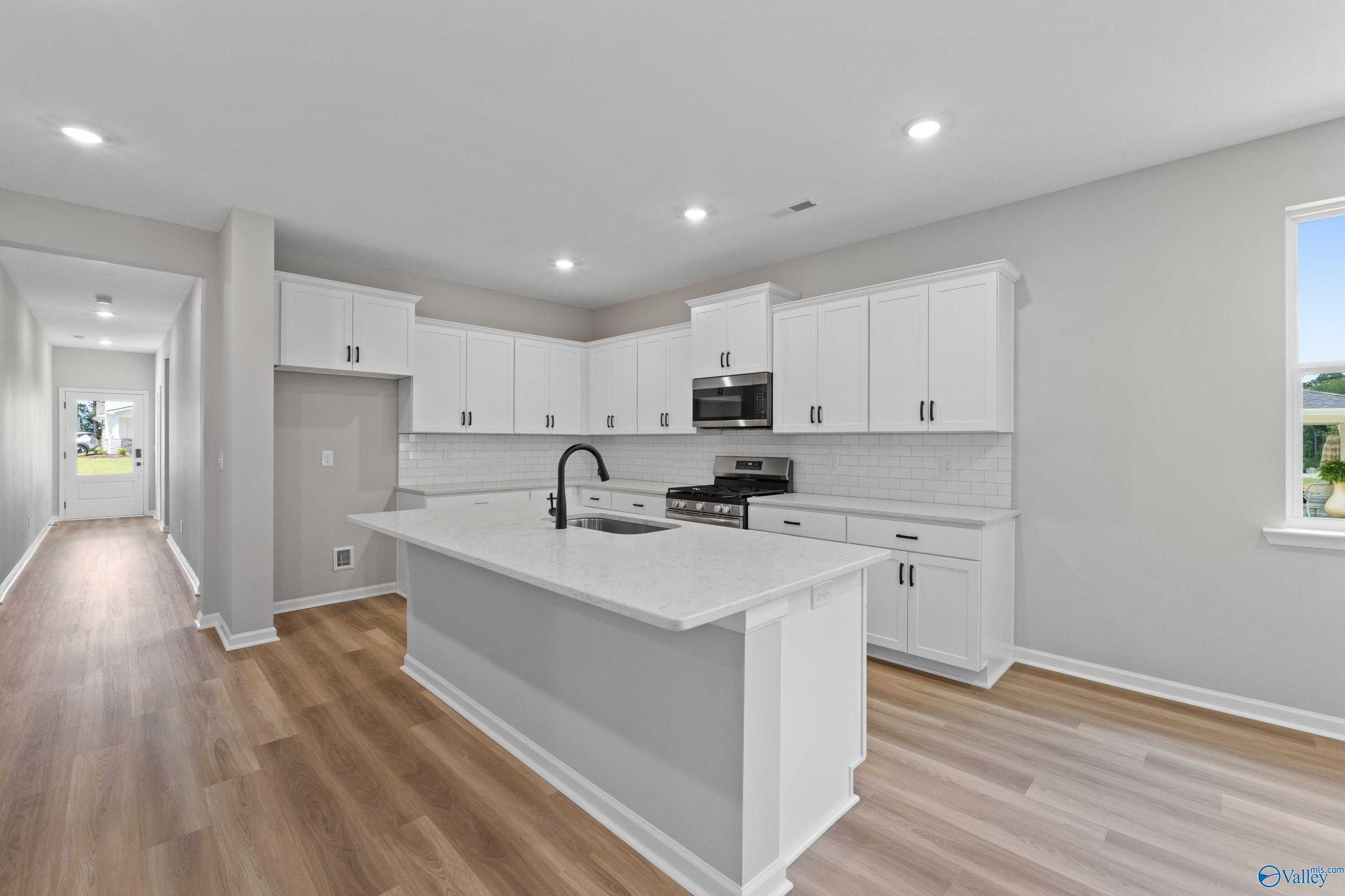 Modern white kitchen with quartz island, subway tile backsplash, and stainless appliances in The Nantucket by Evermore Homes, Madison, AL