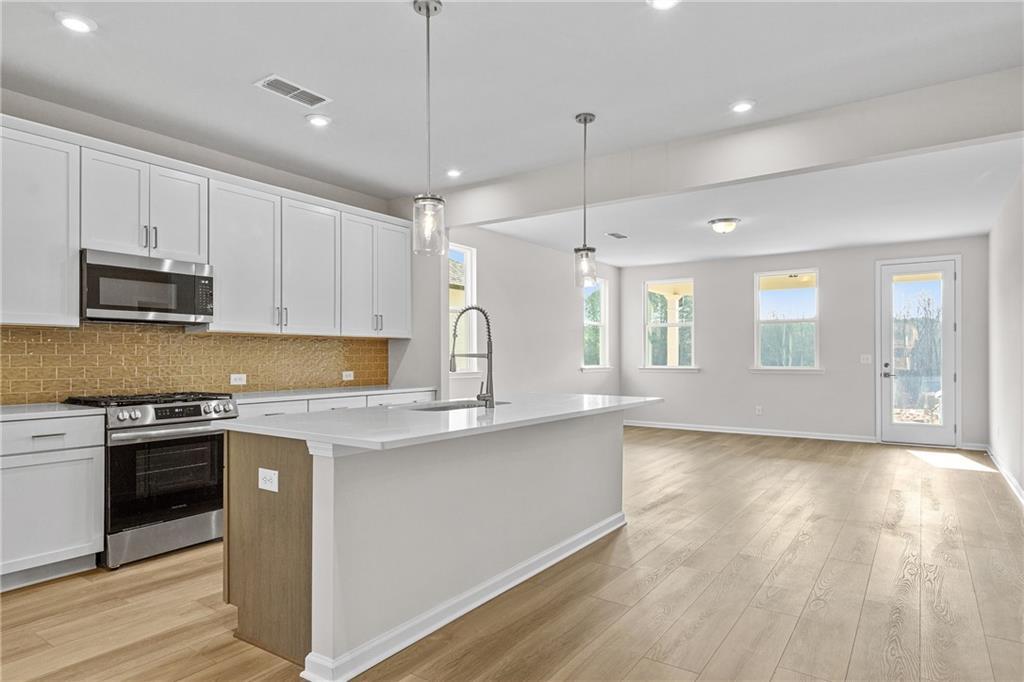 Open-concept kitchen with white cabinets, quartz island, and tile backsplash in The Glenwood B at Kelly Preserve, Loganville.