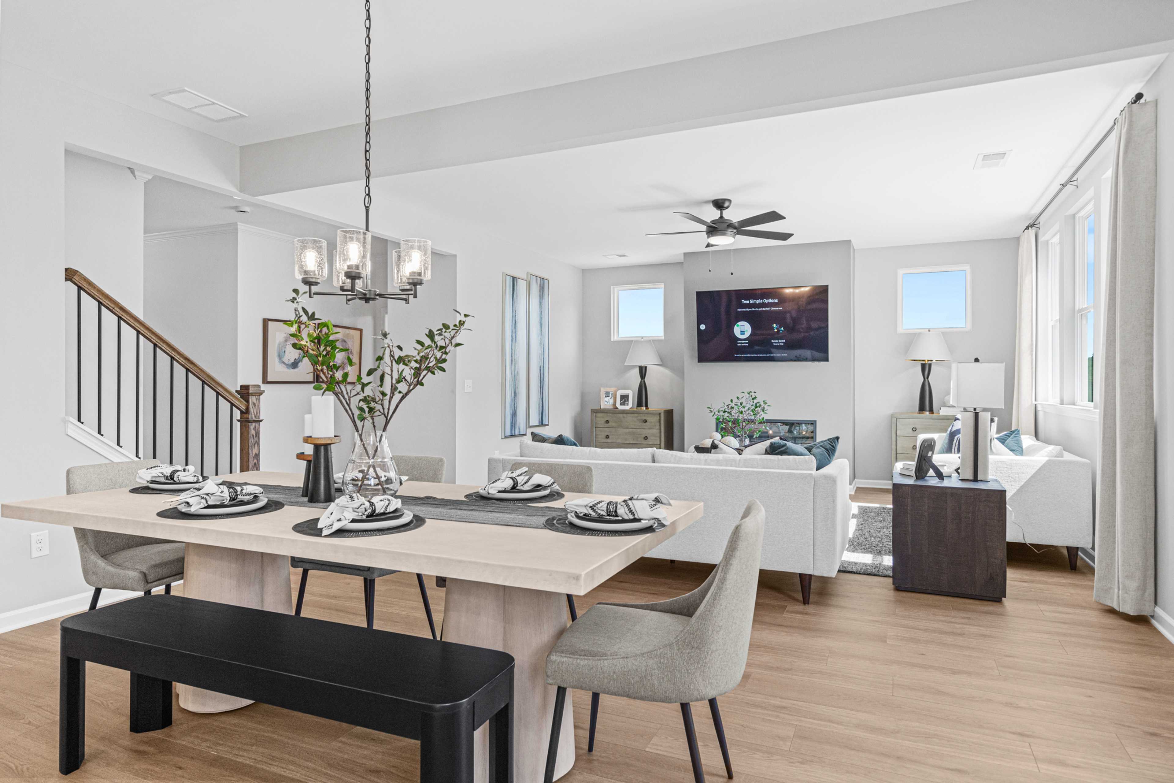Open-concept dining and living room at The Bluffs in Canton, Georgia featuring hardwood floors, white sofa, chandelier, and mounted TV