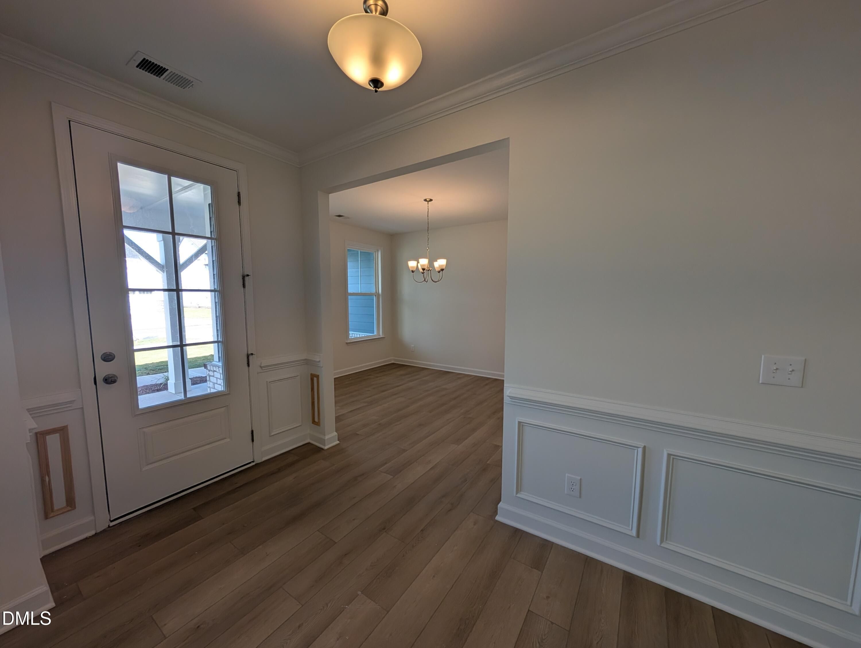 Foyer with glass-paneled front door, wainscoting, and luxury vinyl plank flooring in Davidson Homes The Magnolia A, Wendell Ridge NC