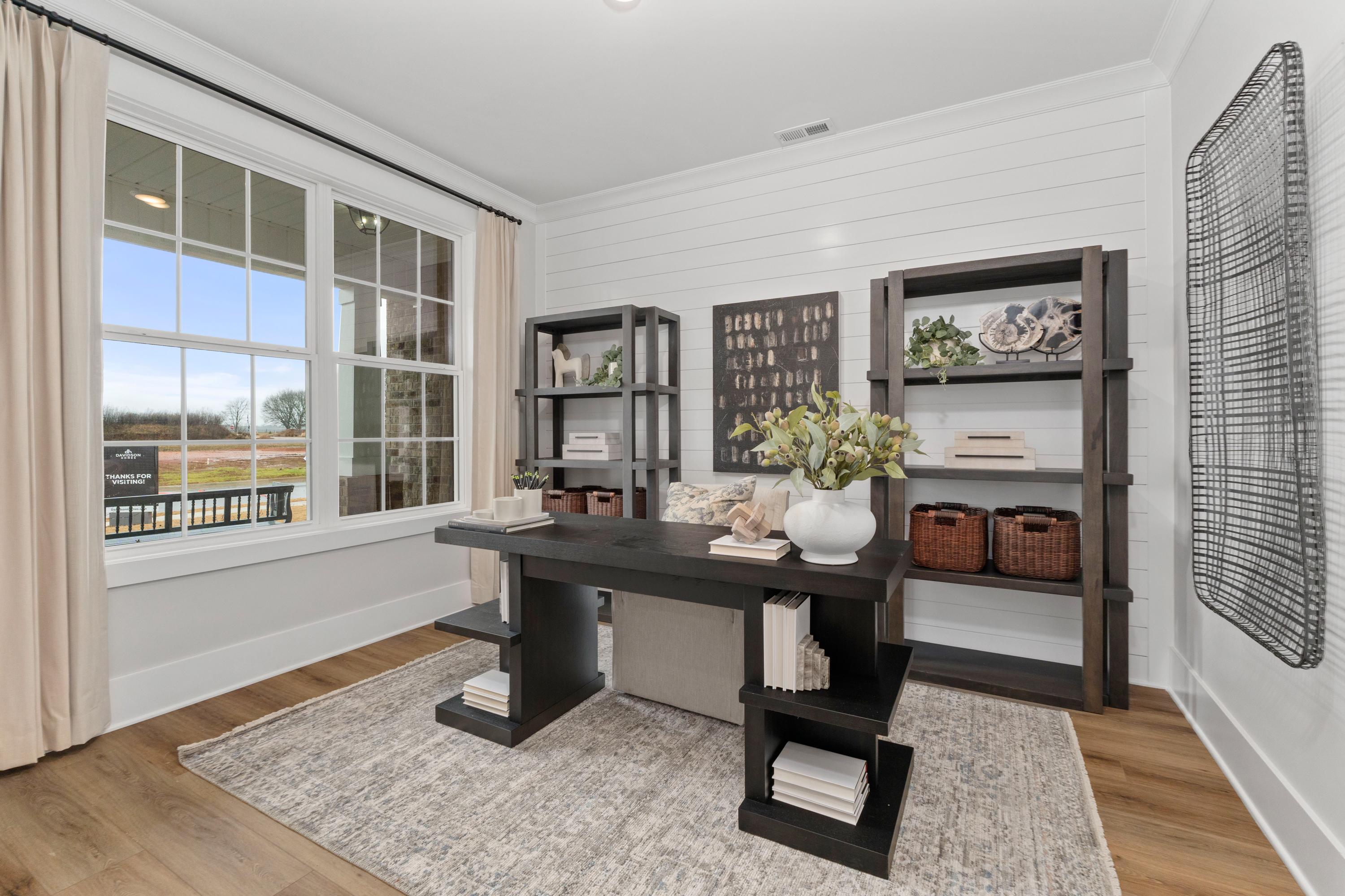 Cozy home office at Little Creek in Arab Alabama featuring dark wood desk, built-in bookshelves, plants, and large windows with wooded view