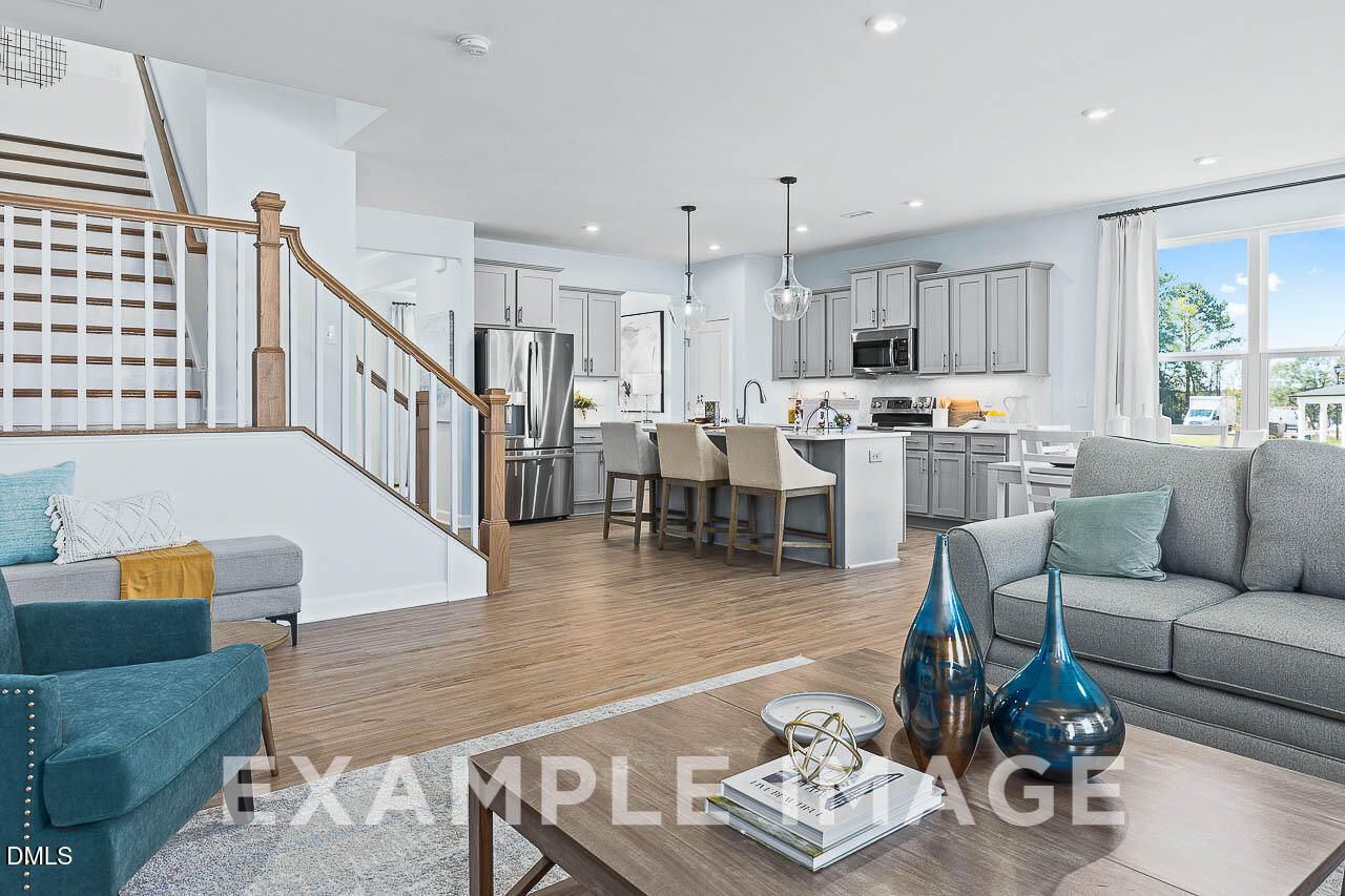 Open-concept living room and kitchen with gray cabinetry, center island, and hardwood floors in The Ash C, Lillington, NC