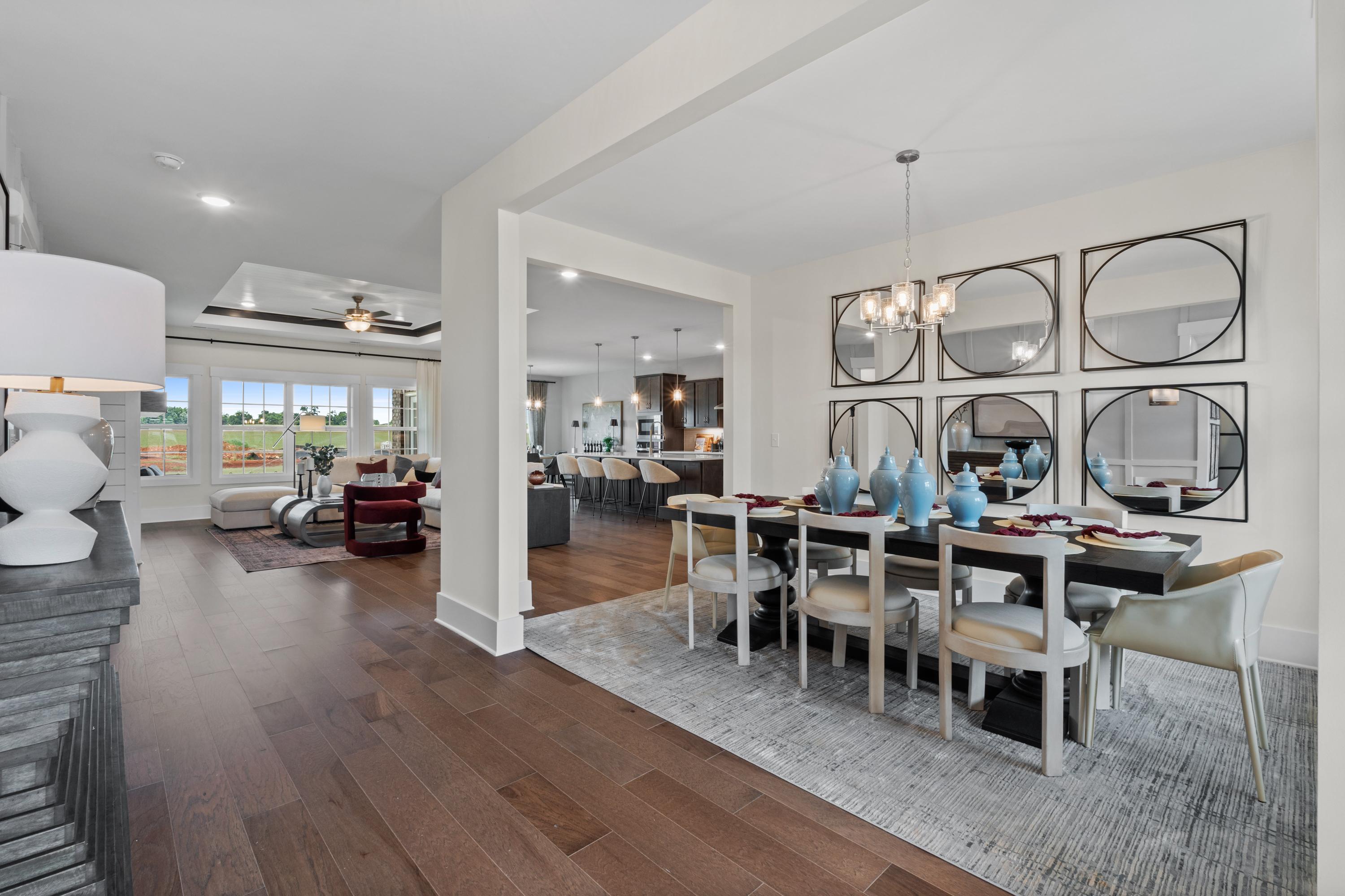 Spacious open-concept living and dining room at Creekside in Harvest, Alabama with hardwood floors, mirrored wall, and chandelier