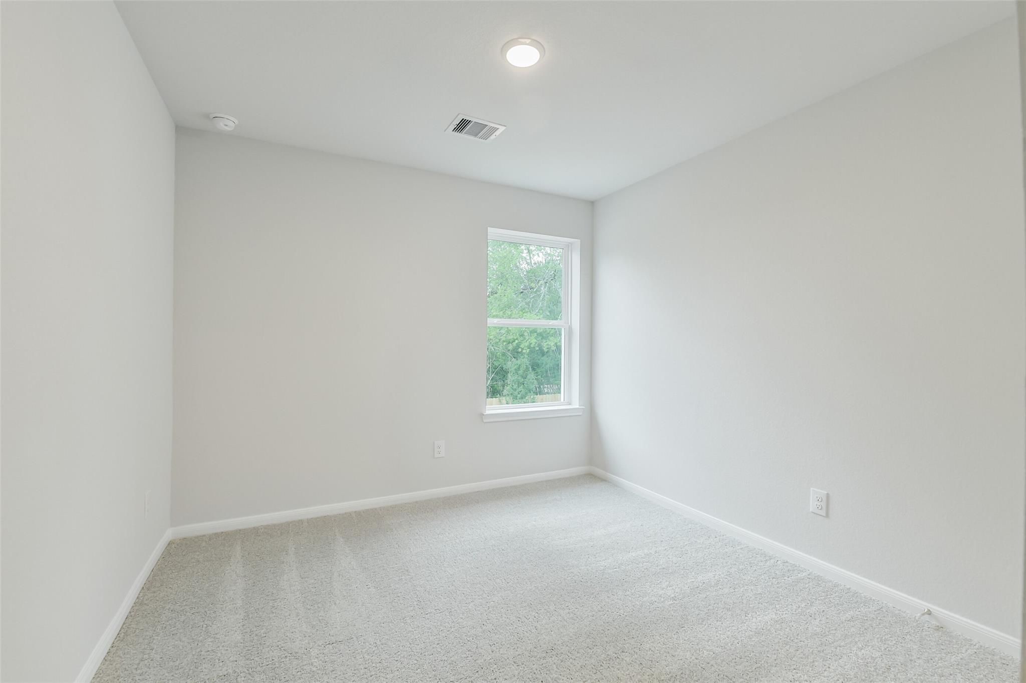 Empty secondary bedroom with light gray walls, carpeted floor, and large window in Davidson Homes The Brazos F, Conroe, Texas