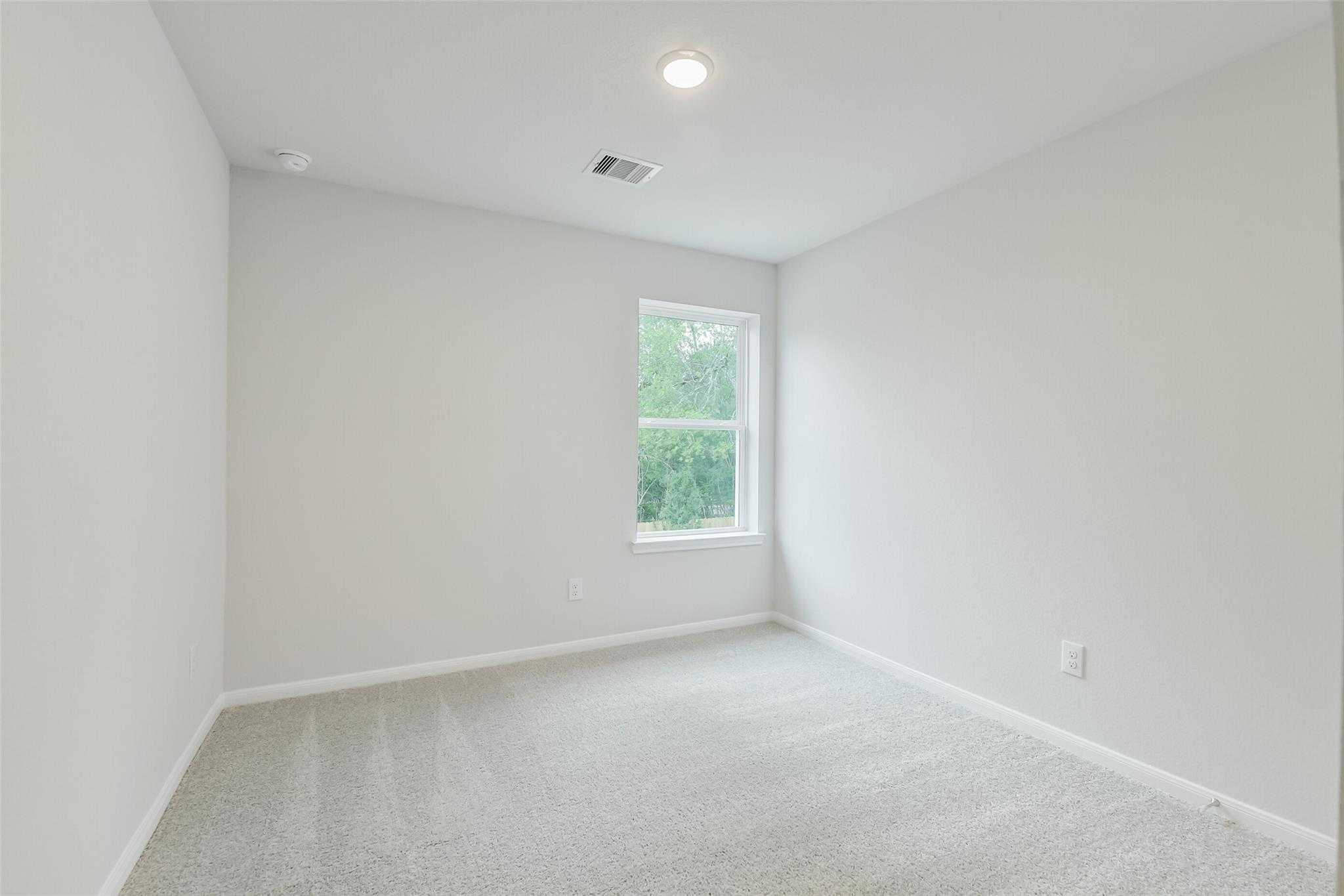Empty secondary bedroom with light gray walls, carpeted floor, and large window in Davidson Homes The Brazos F, Conroe, Texas