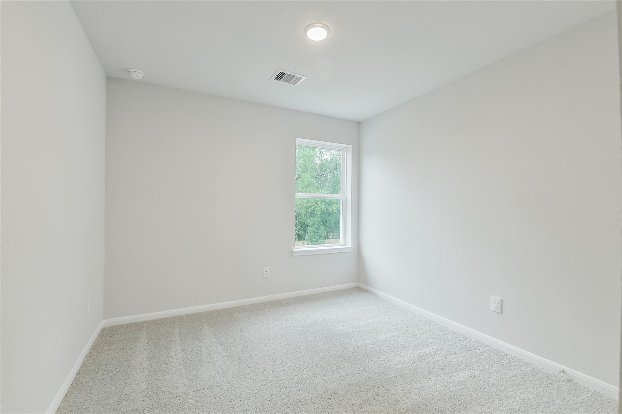 Empty bedroom with light gray walls, beige carpet, large window overlooking trees in 5-bedroom Davidson Homes The Brazos F, Conroe, Texas