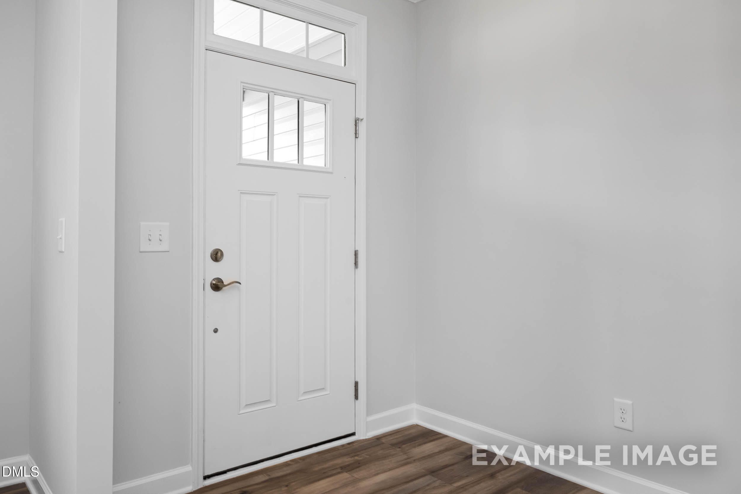 Welcoming foyer with white paneled entry door, sidelight window, gray walls, and hardwood floors in Davidson Homes The Ash B, Lillington, NC