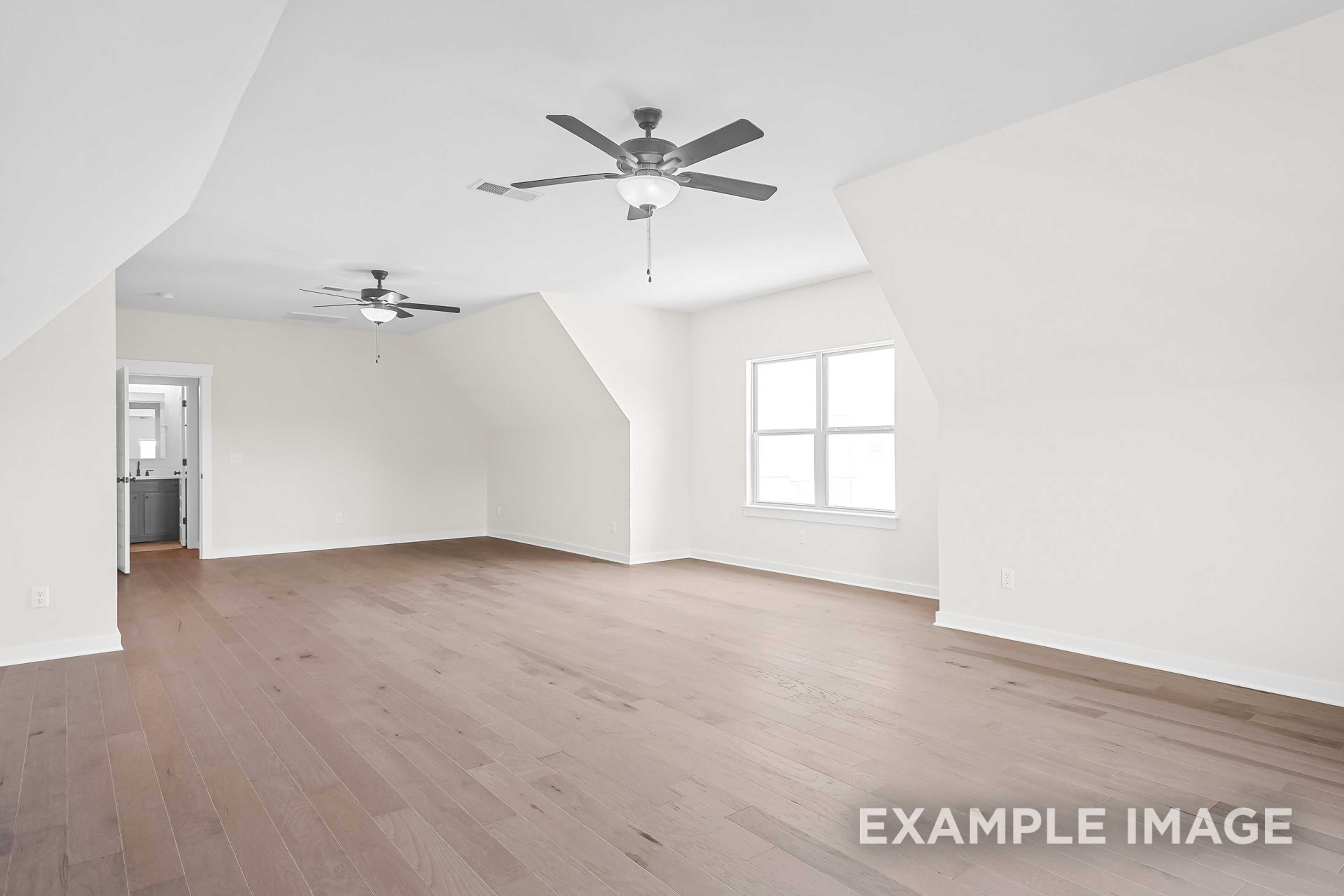 Spacious upstairs bonus room in The Hawkins home design with vaulted ceilings, dual ceiling fans, large windows, hardwood floors, and adjacent bathroom