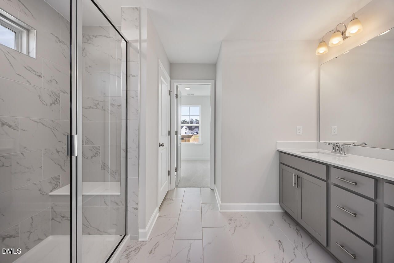 Elegant master bathroom with frameless glass shower, marble tiles, and double gray vanity in Davidson Homes The Willow G, Angier, NC