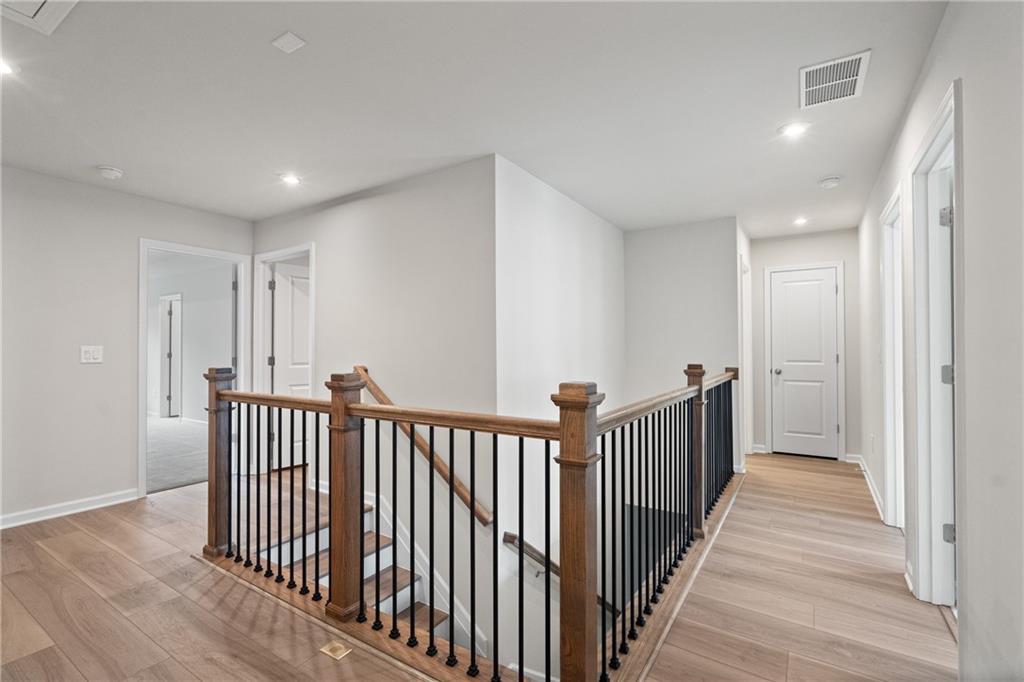 Bright upstairs hallway with oak hardwood floors, wooden staircase, and black metal railings in Davidson Homes The Marion B, Kennesaw, GA