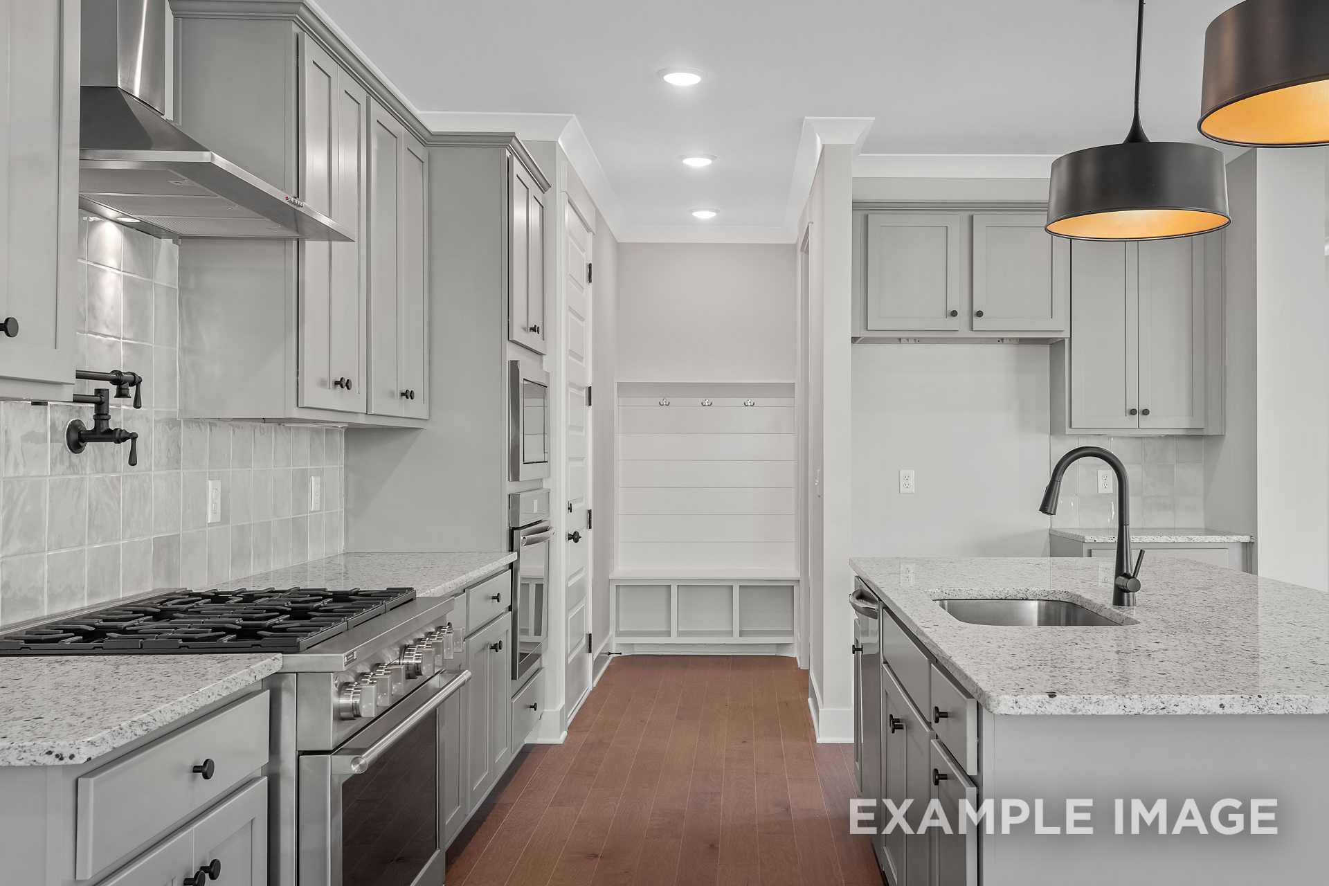 Spacious kitchen in The Hathaway home with white shaker cabinets, quartz island sink, gas range, subway tile backsplash, hardwood floors, and mudroom view