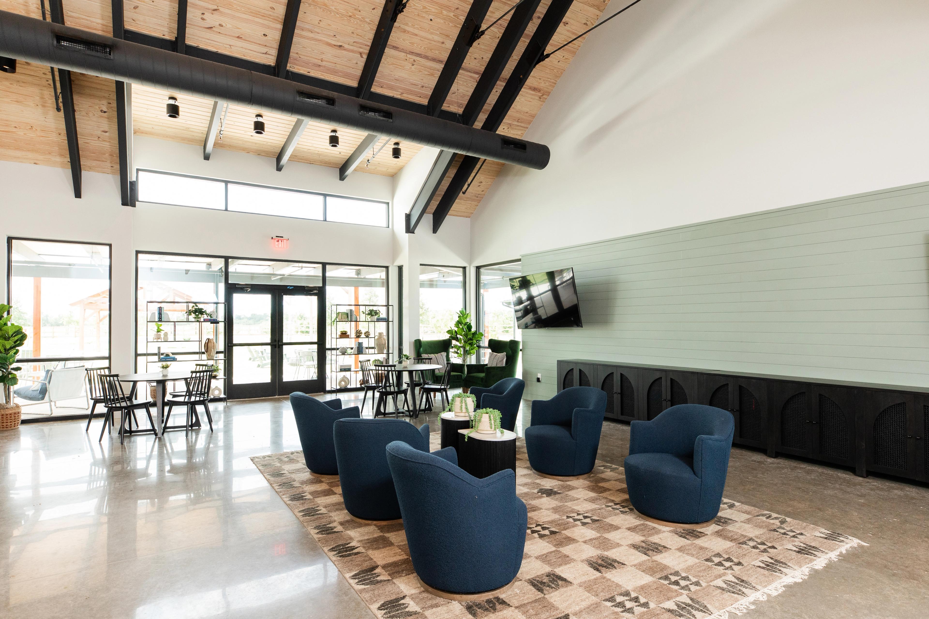 Inviting lounge area at Emberly in Beasley Texas with blue armchairs wooden beam ceiling green accent wall and large windows