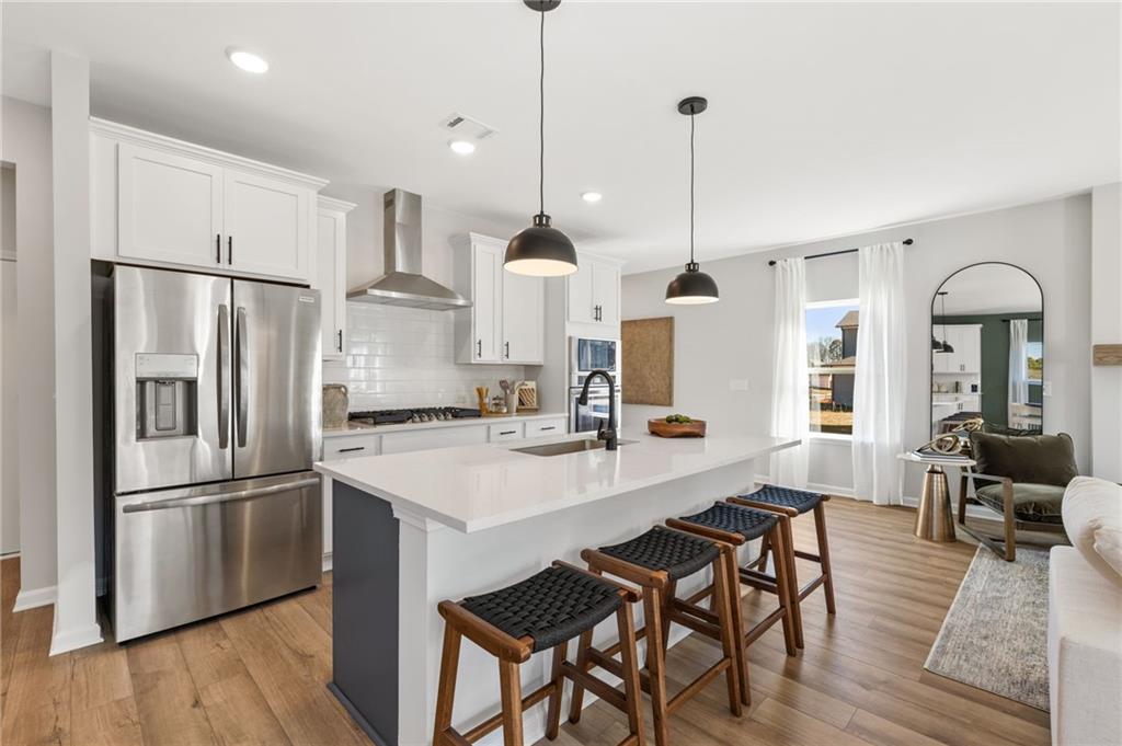 Modern open-concept kitchen with white shaker cabinets, quartz island, stainless fridge, and black pendant lights in Davidson Homes Rabun B, Canton GA