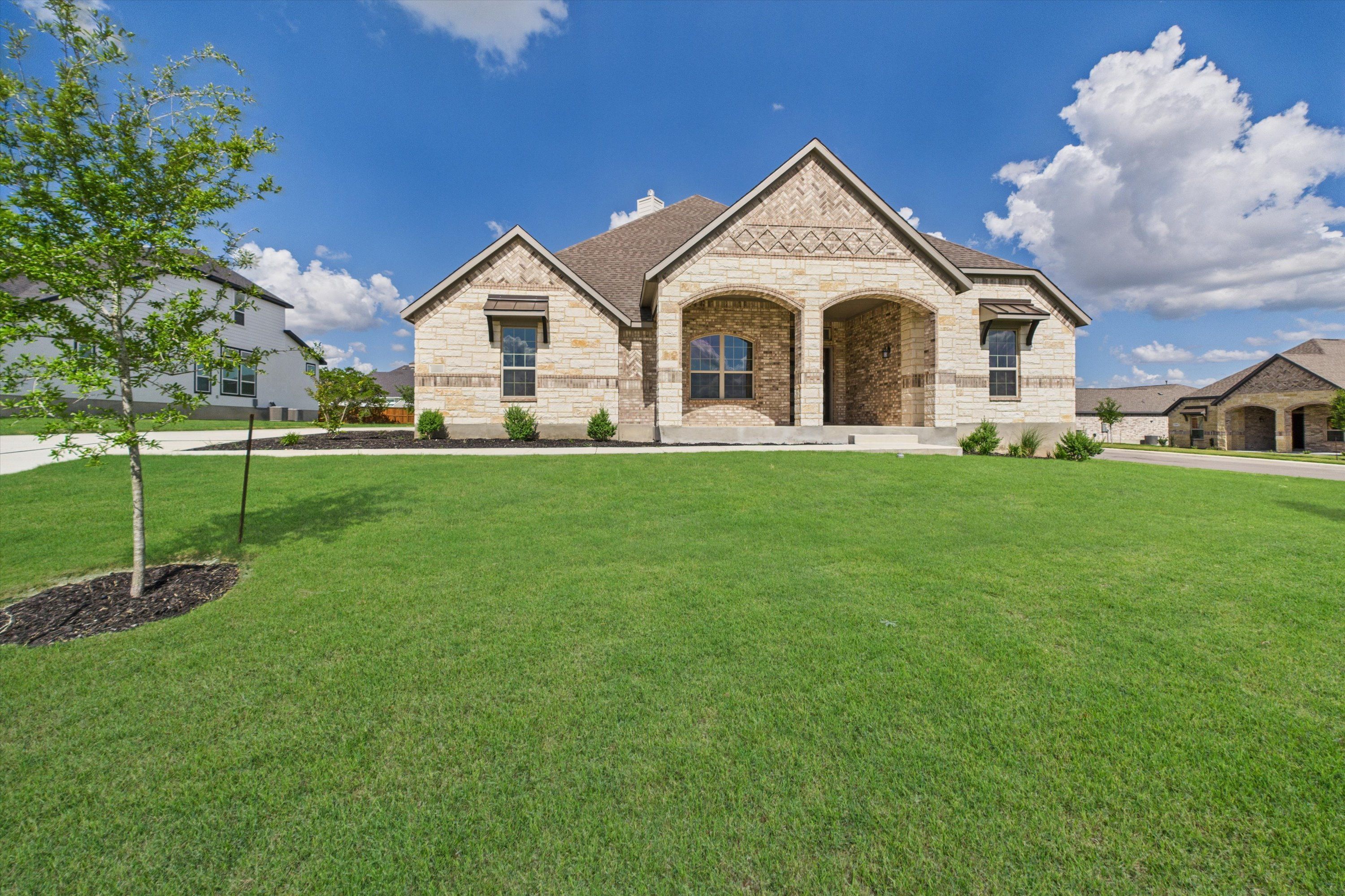 Modern stone-brick single-story home with arched porch, lush green lawn in Potranco Oaks, Castroville, Texas - Davidson Homes Summerlin C