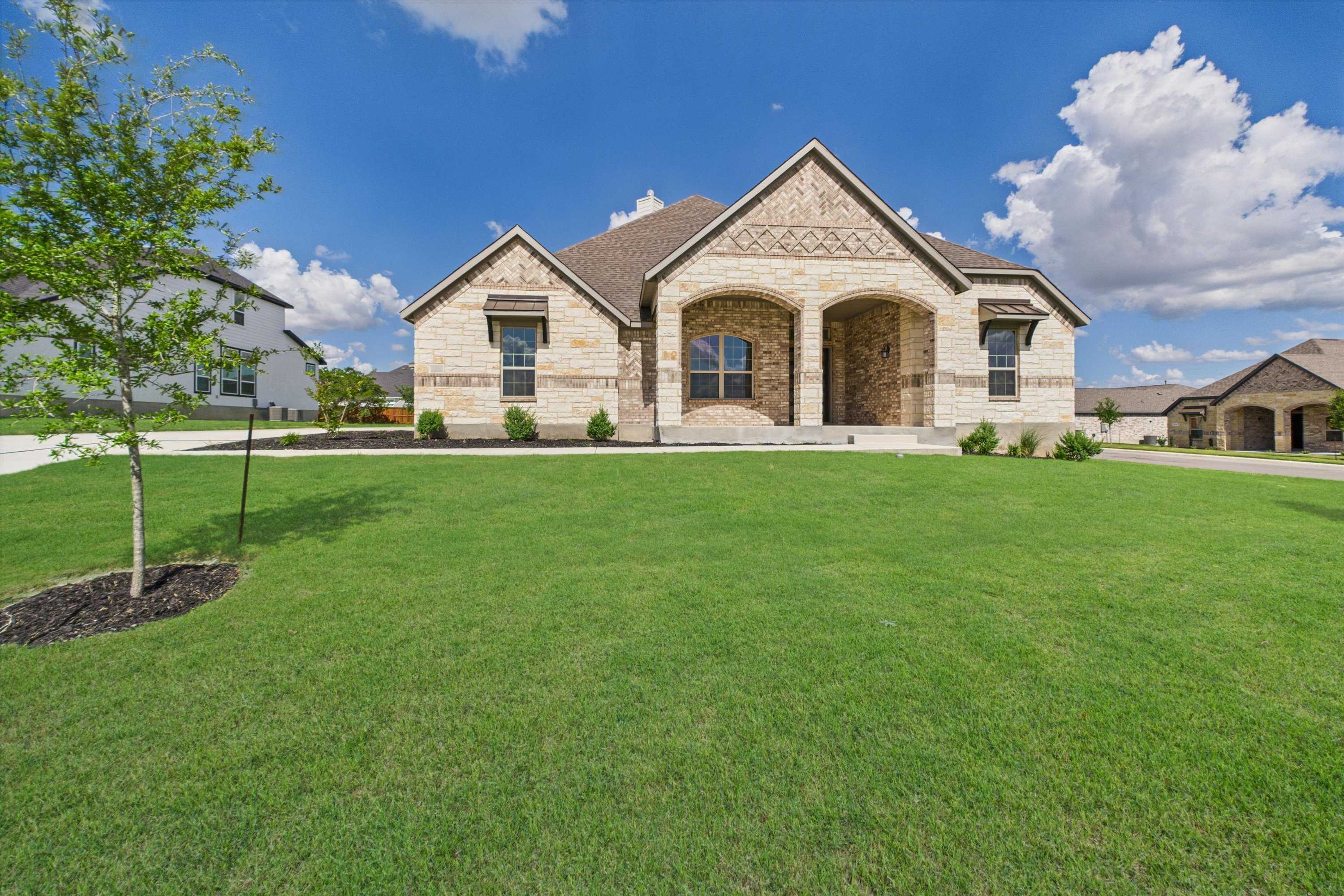 Modern stone-brick single-story home with arched porch, lush green lawn in Potranco Oaks, Castroville, Texas - Davidson Homes Summerlin C