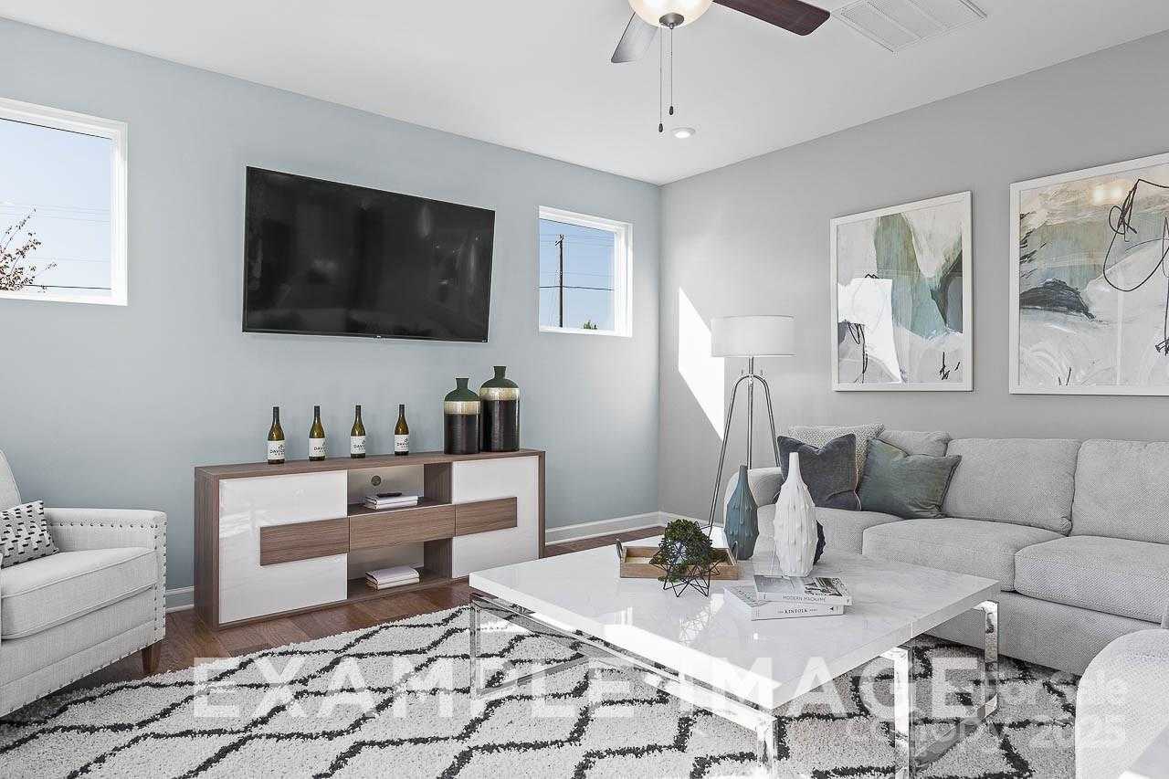 Modern living room with gray sectional sofa, mounted TV, abstract wall art, and natural light in The Hemlock A by Davidson Homes, Belmont, NC