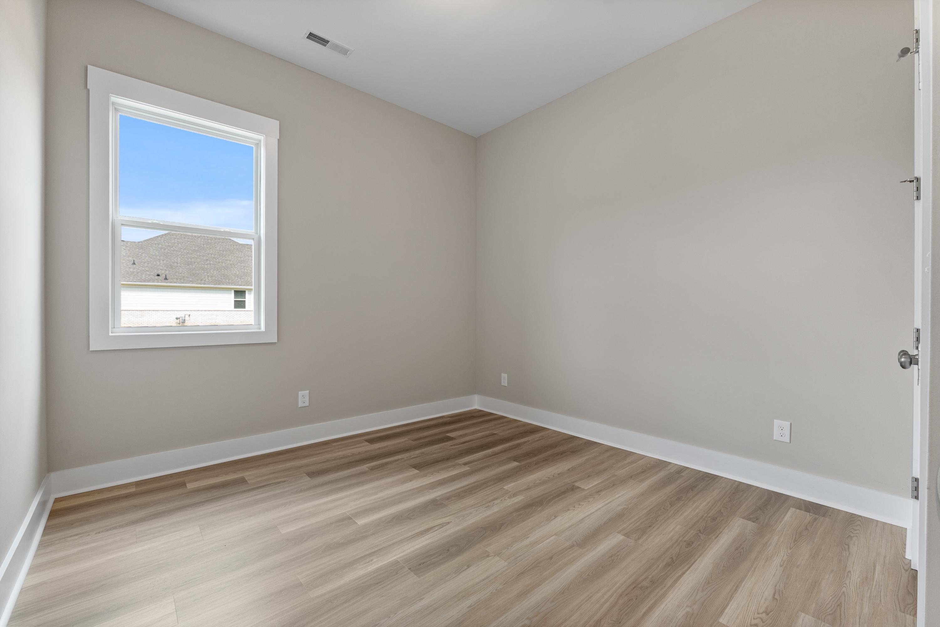Spacious secondary bedroom in The Oxford C with neutral gray walls, oak laminate floors, and large window view