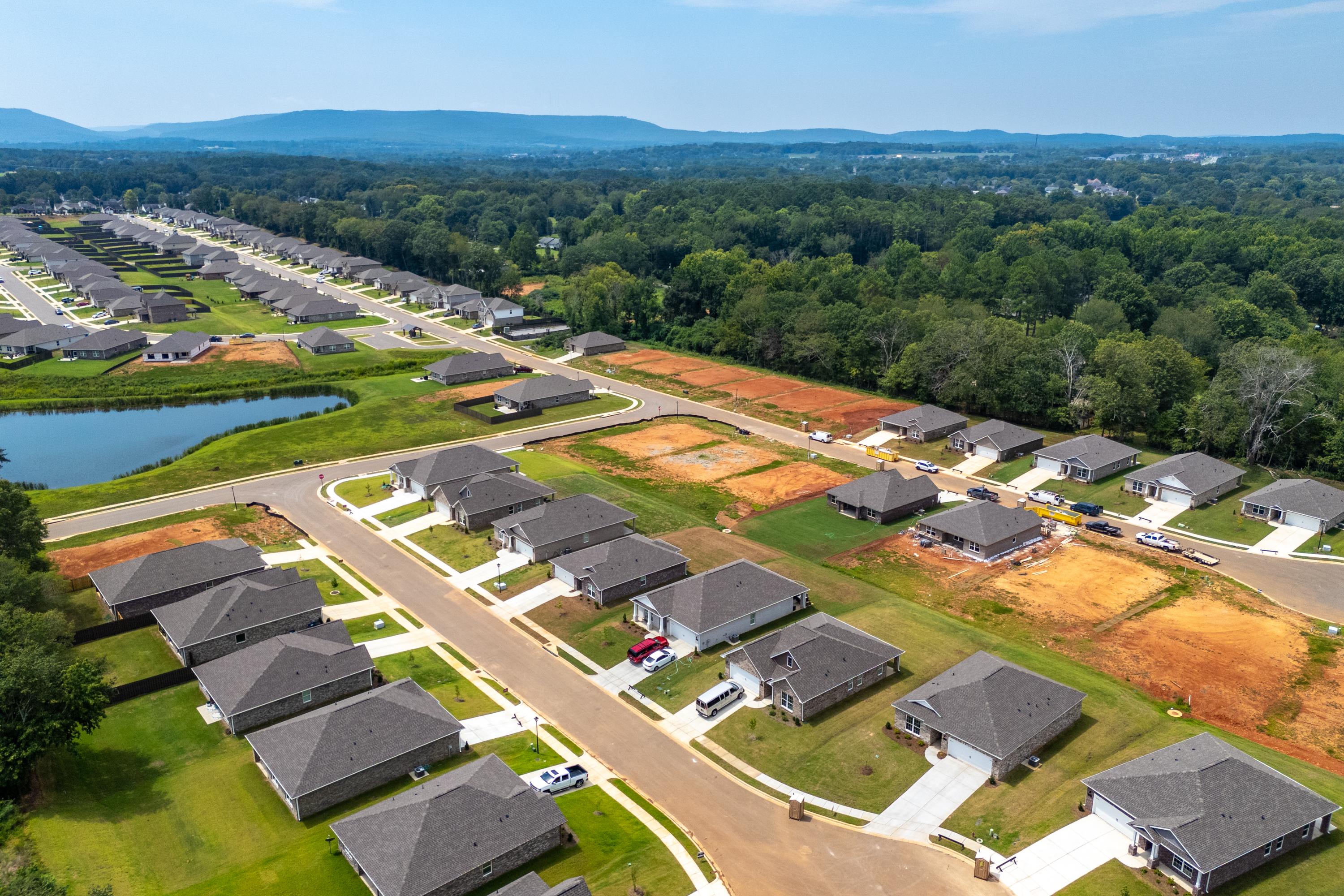 Aerial view of Flint Meadows neighborhood in New Market Alabama with new homes construction sites pond and wooded hills