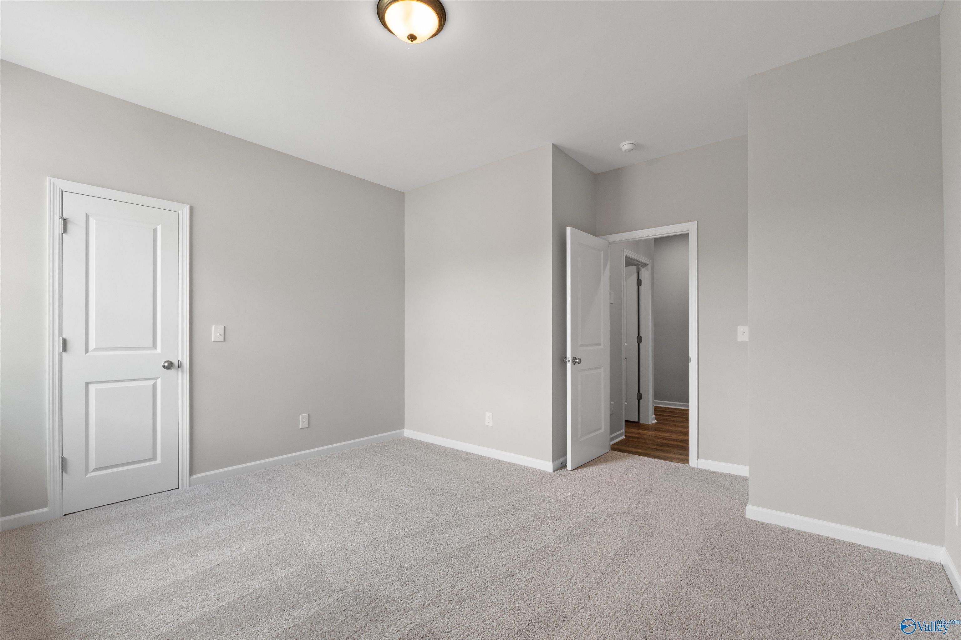 Bright secondary bedroom with light gray walls, neutral carpet, and open door to ensuite in Davidson Homes The Luna, Hazel Green, AL