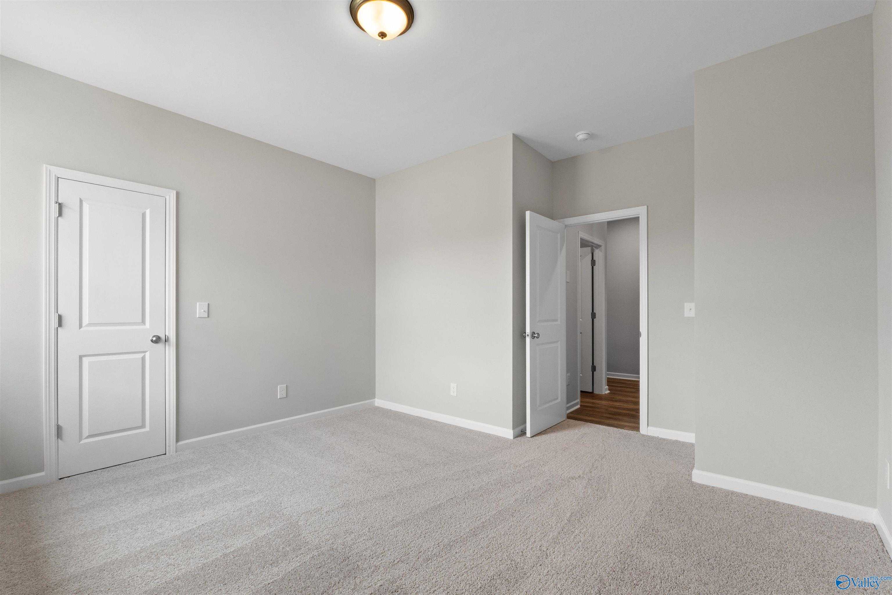 Bright secondary bedroom with light gray walls, neutral carpet, and open door to ensuite in Davidson Homes The Luna, Hazel Green, AL