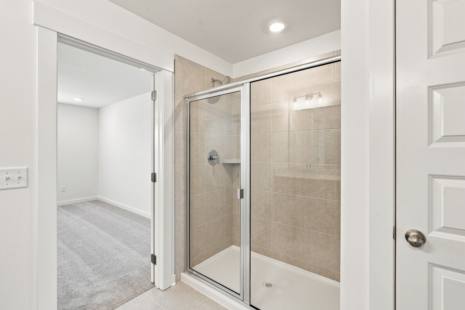 Glass-enclosed tile walk-in shower in bright bathroom with adjoining carpeted bedroom in Davidson Homes' Willow C, Gallatin, TN
