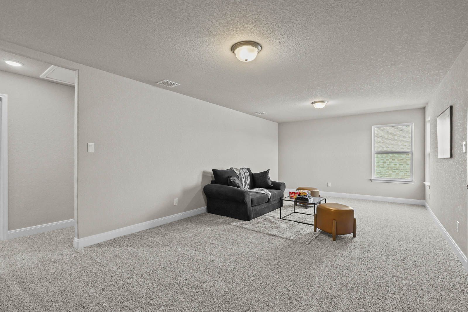 Spacious carpeted game room in The Jennings G floor plan featuring neutral walls, natural light, and comfortable seating.