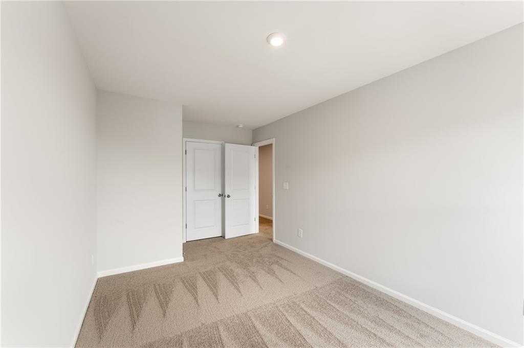 Spacious secondary bedroom with light gray walls, white double doors, and beige patterned carpet in Davidson Homes The Monroe A, Emerson, Georgia