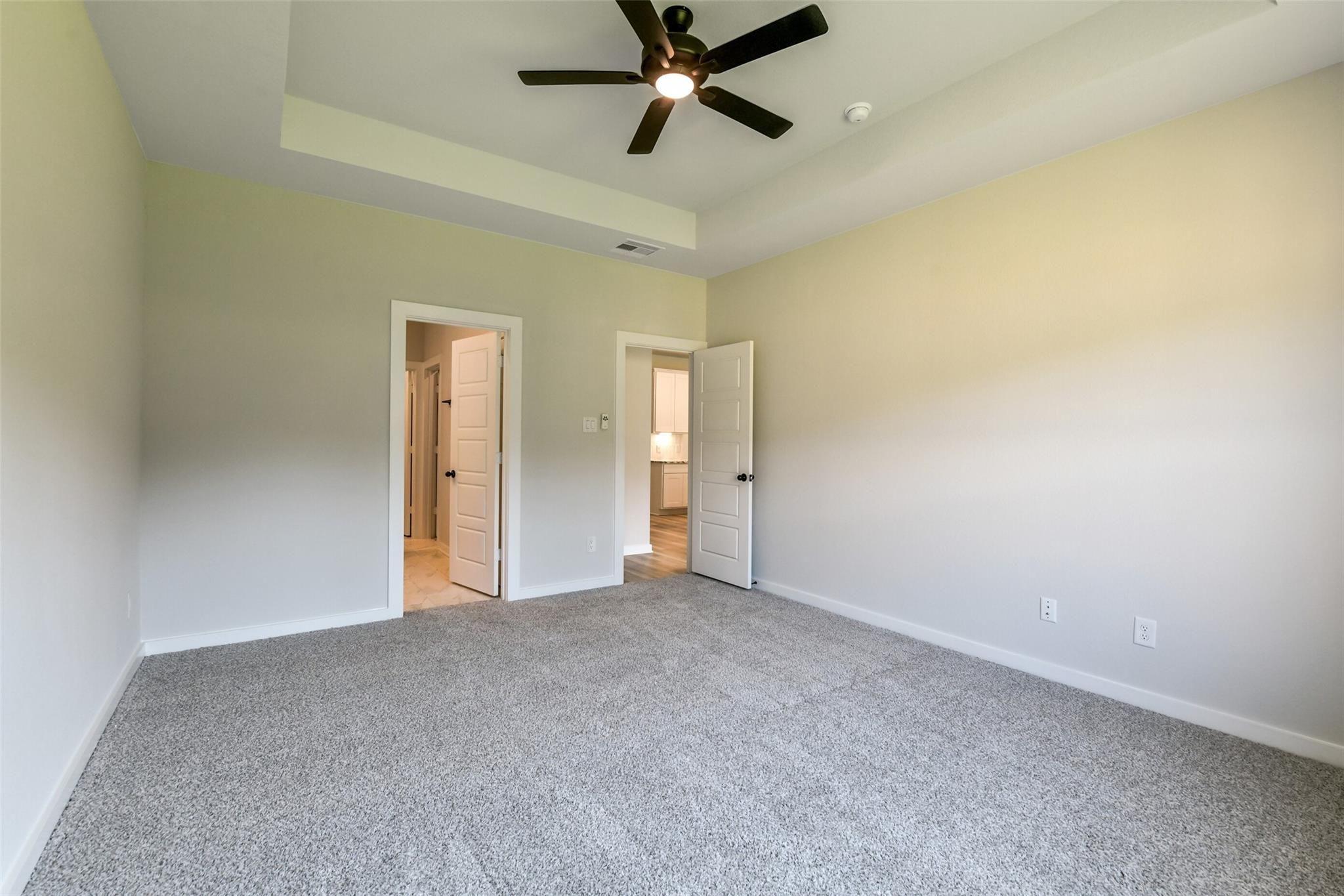 Spacious bedroom with ceiling fan, light walls, carpeted floor, and adjacent bath doors in Davidson Homes The Daphne H, Crosby, Texas