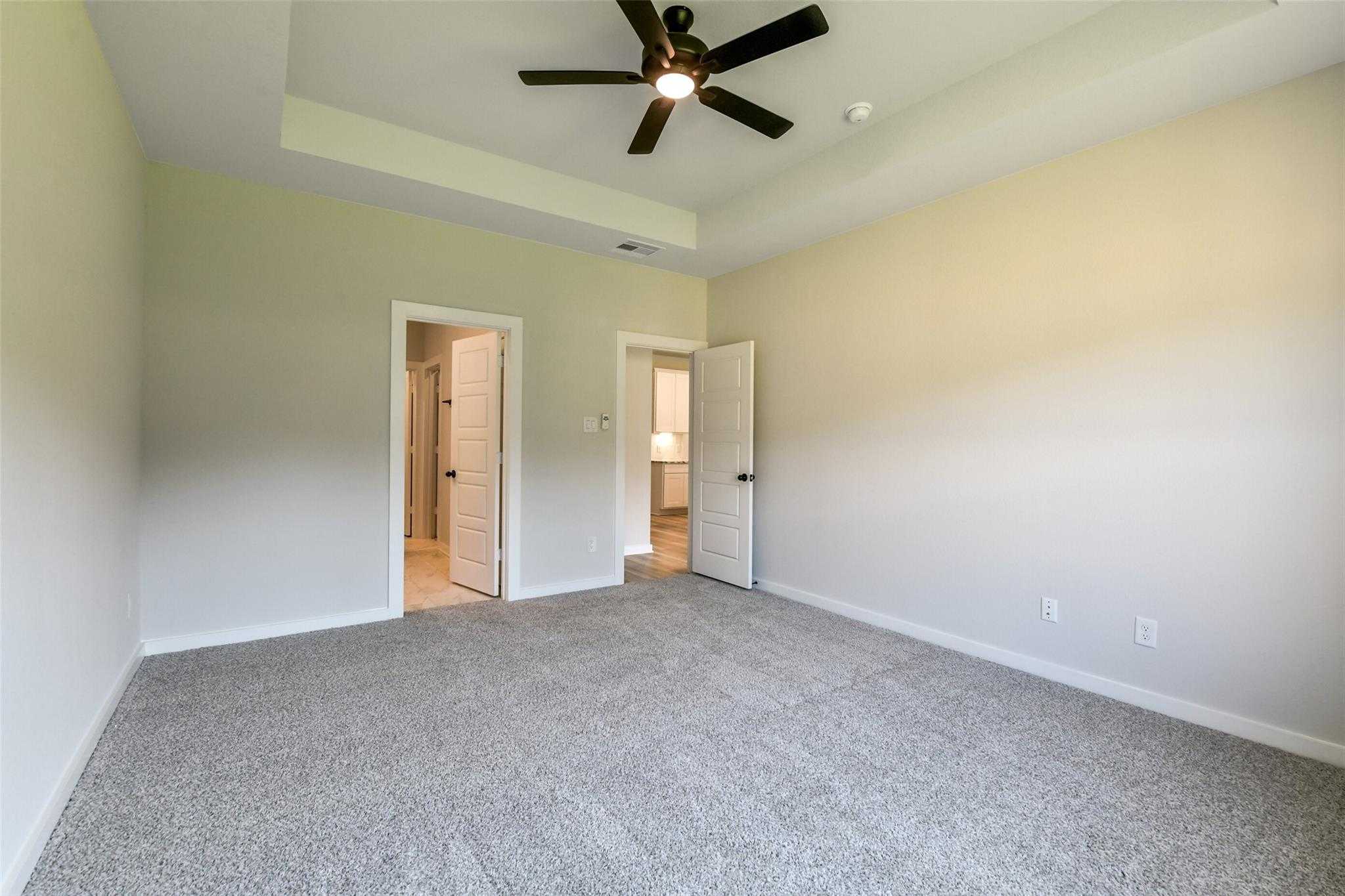 Spacious bedroom with ceiling fan, light walls, carpeted floor, and adjacent bath doors in Davidson Homes The Daphne H, Crosby, Texas