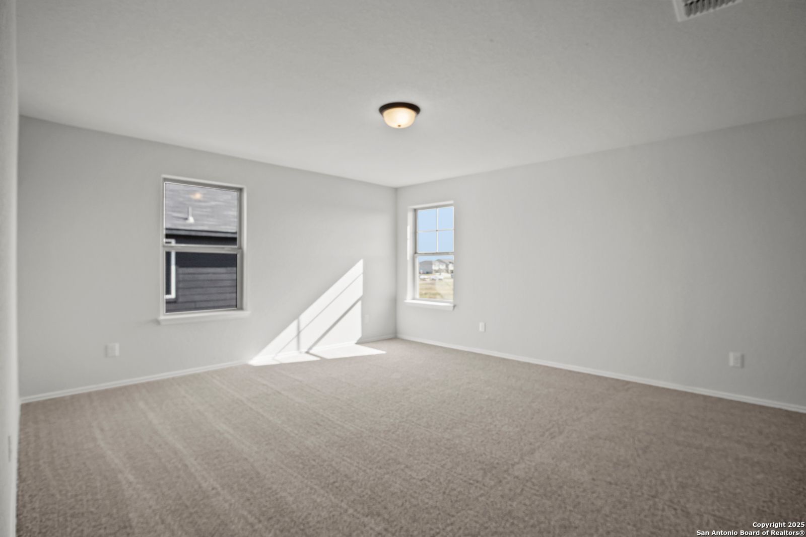 Bright empty bedroom with light gray walls, beige carpet, large windows, and natural light in Davidson Homes The Douglas C, Seguin, Texas